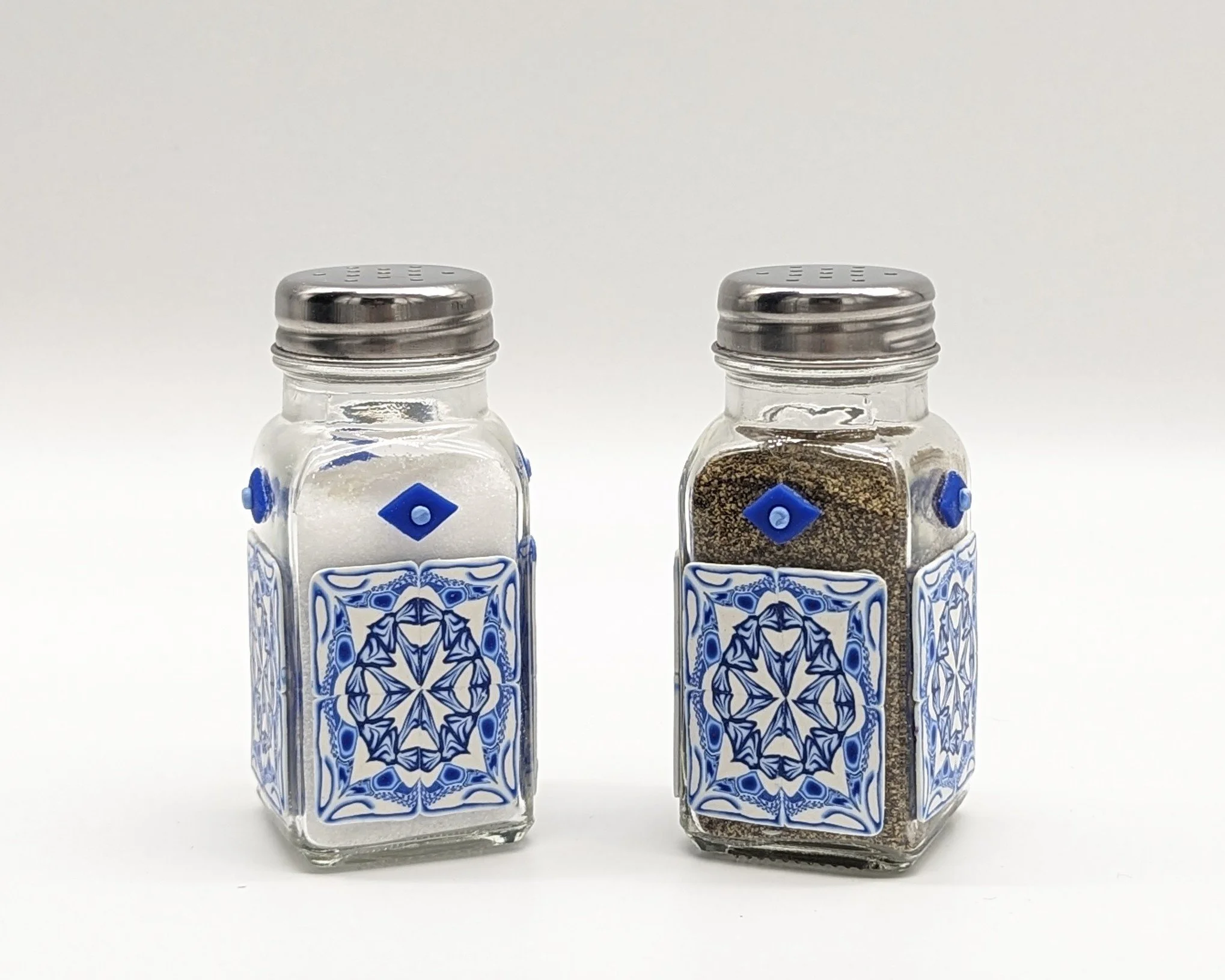 🔴 Sold: 
Blue and White Delft-Style Salt and Pepper Shakers by Art Illusions by Young, Folsom, Louisiana. This elegant matching pair of glass salt and pepper shakers is beautifully decorated with hand-sculpted and painted polymer clay in classic blu