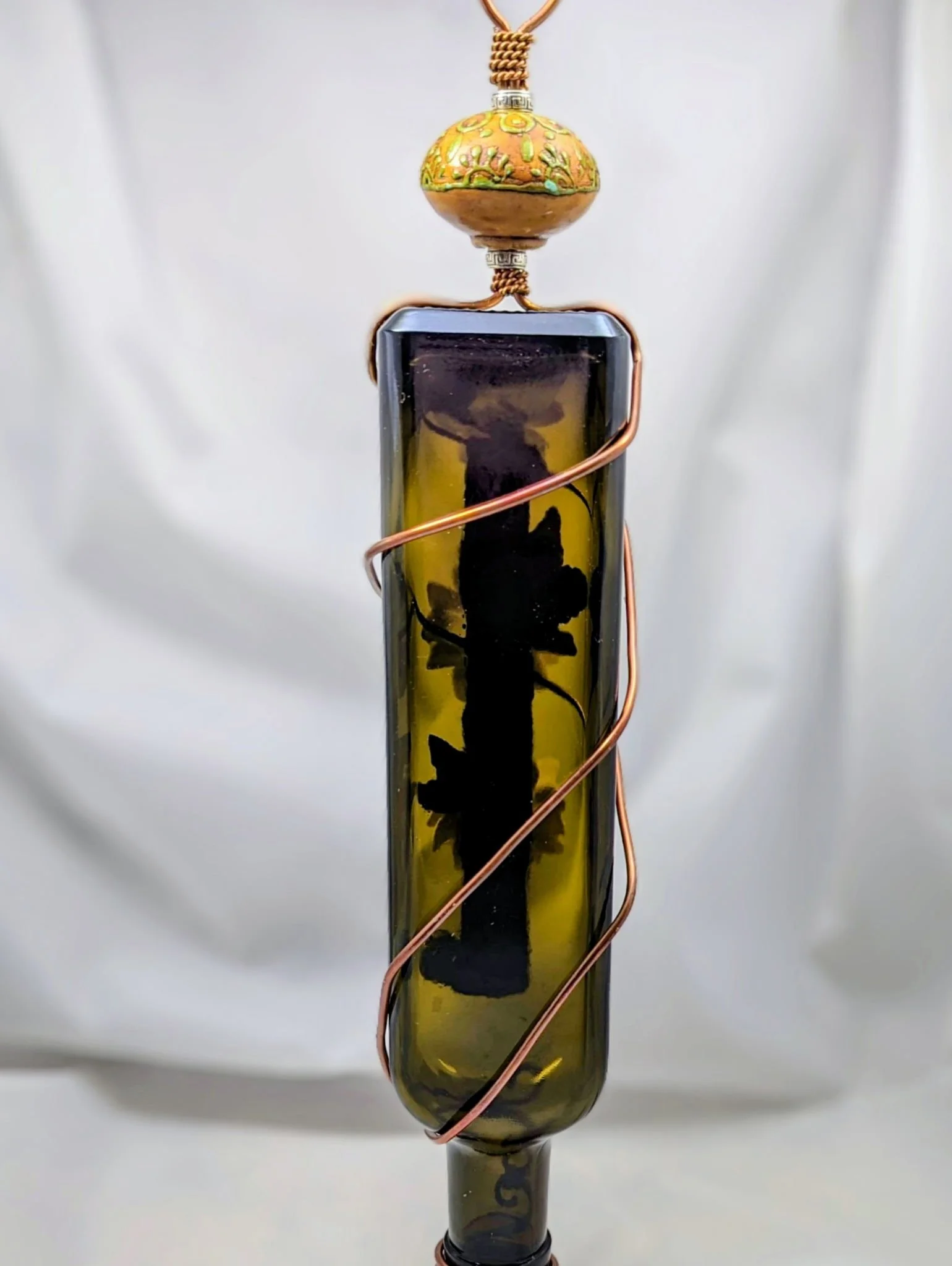 Decorative glass hummingbird feeder by Art Illusions by Young featuring a vertical glass bottle, wrapped with copper wires, and topped with a spherical knob ornament.
