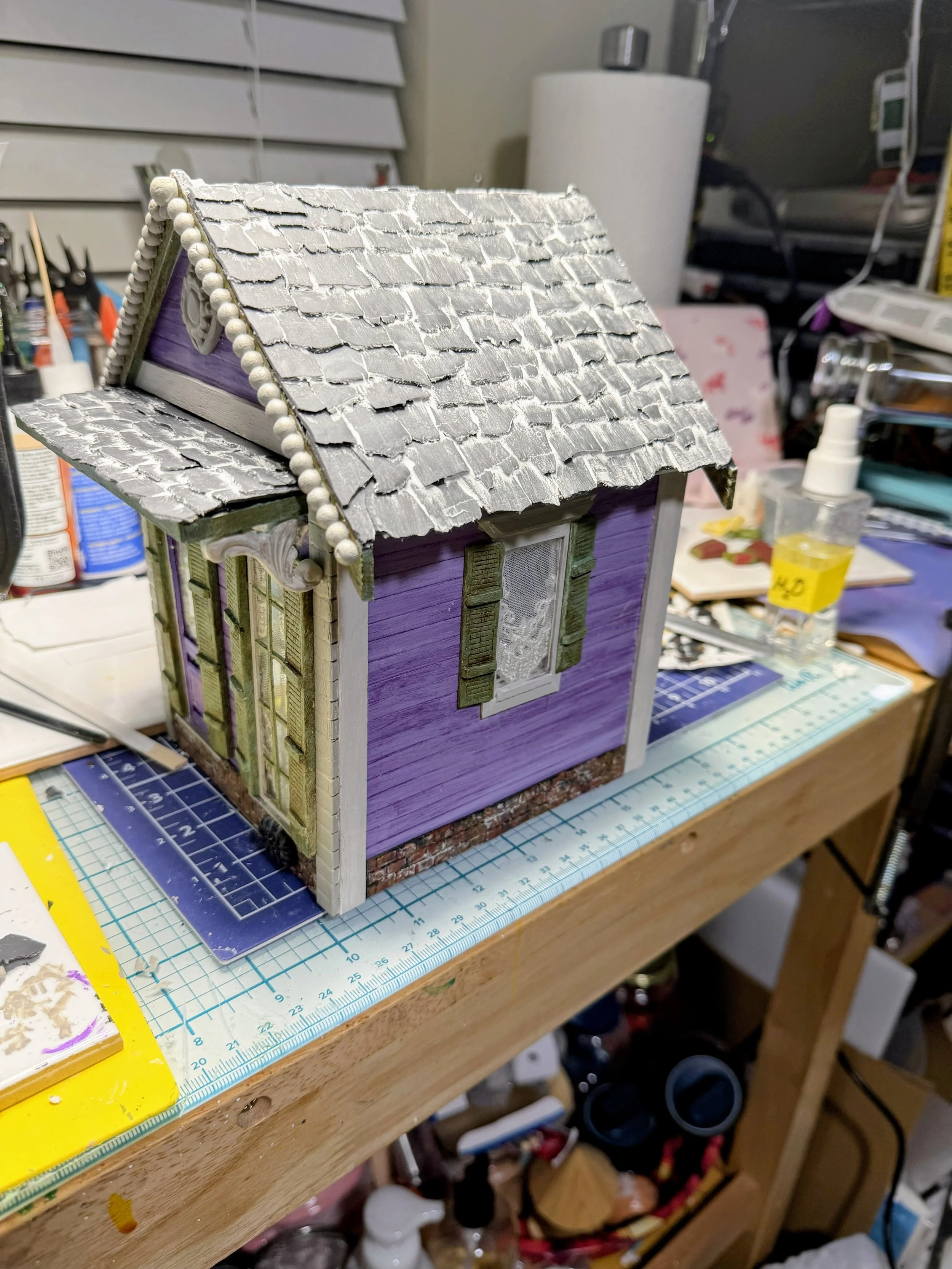 Purple Reign Shotgun House diorama on the studio workbench by Art Illusions by Young. When completed the full lavender shotgun house with black fence, lush yard, and functional tissue dispensing roof is ready as a collectible mixed media functional a