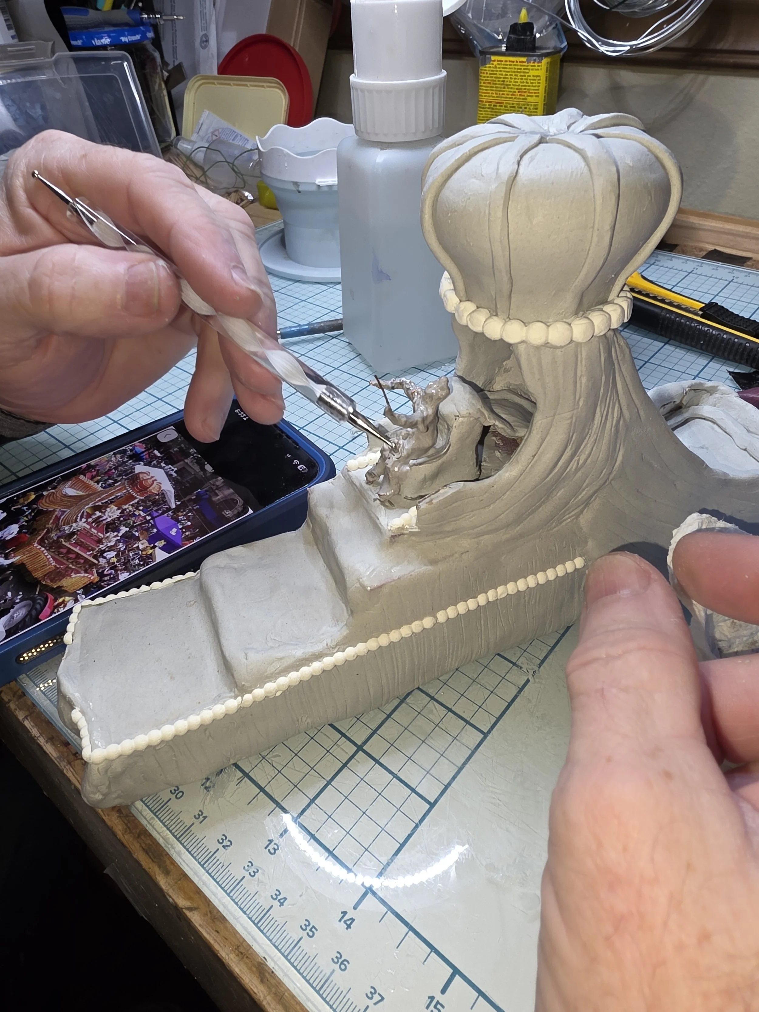 Hands carefully sculpting clay human figures for the King Rex Mardi Gras float. Studio creation process showing detailed clay work by Art Illusions by Young in Folsom, Louisiana.