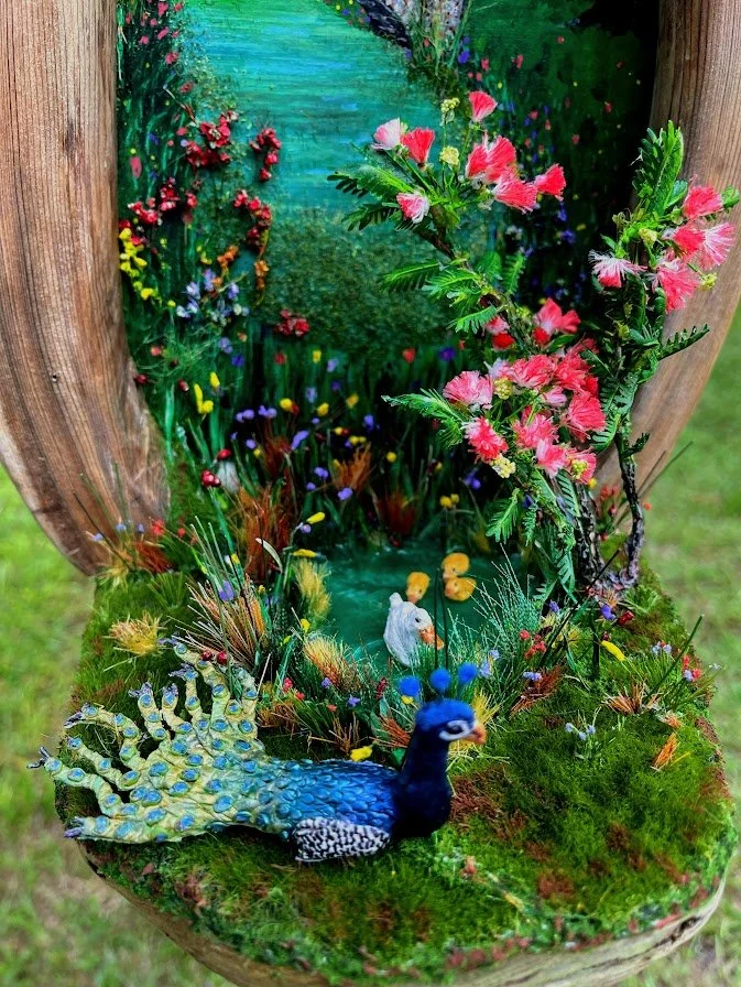 Dramatic angled view of the Enchanted City Park Serenity diorama with the hollow cypress trunk filled with a miniature pond, duck and ducklings, peacock, bridge, and lush pink mimosa flowers. One-of-a-kind mixed media micro landscape by Art Illusions