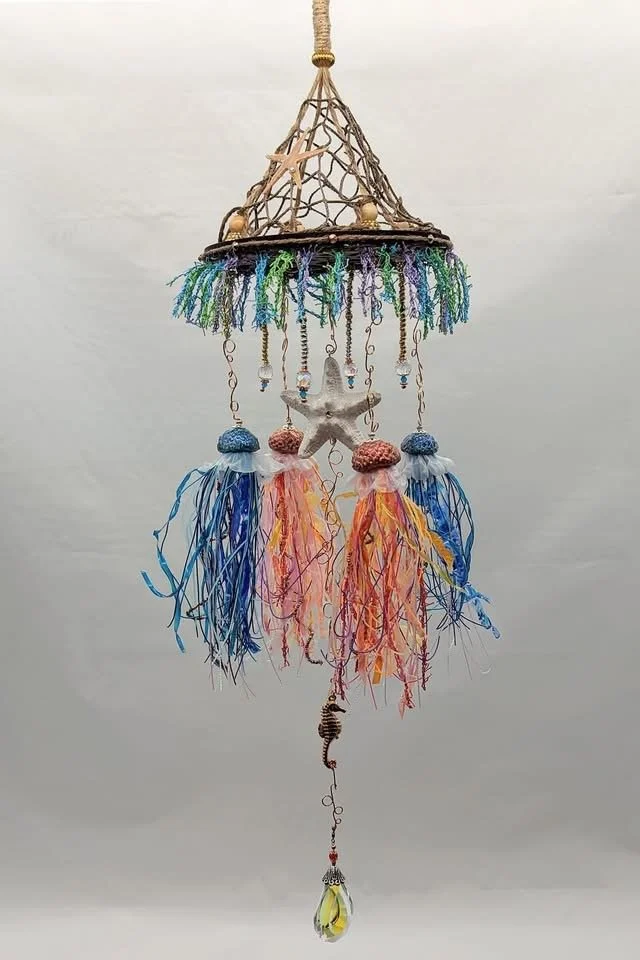 Frontal view of the Jellyfish Mobiles – Chihuly-Inspired Light Catcher by Art Illusions by Young. The scrollwork wooden hanger supports a decorative netted canopy beneath which four handcrafted sea urchin jellyfish with flowing tentacles and iridesce