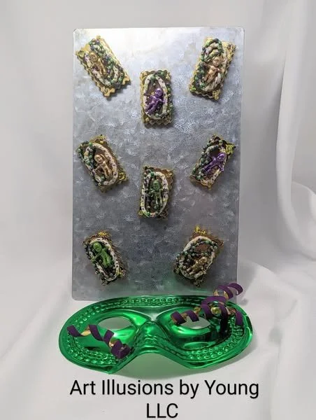 Display card featuring a set of Mardi Gras King Cake Baby magnets/pins by Art Illusions by Young. Each hand painted baby is individually crafted and nestled in a hand-sculpted clay king cake with metallic bead accents in Carnival colors. Shown on a m