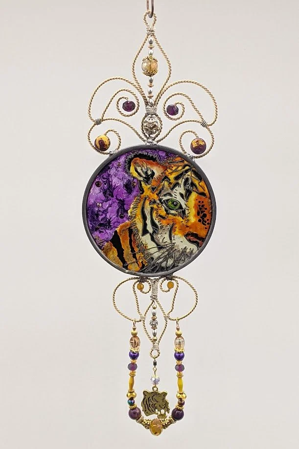 Tiger Illusion Glass by Art Illusions by Young, Folsom, Louisiana. Hand-painted leaded glass round pendant featuring a majestic tiger in a vibrant purple and orange wire topper and dangling bead and crystal accents.