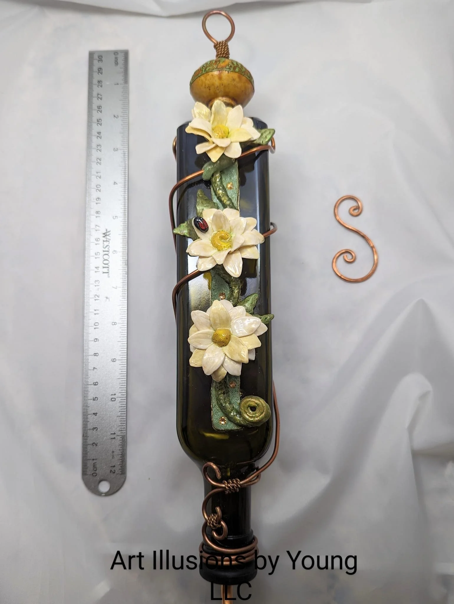 Decorative hummingbird feeder by Art Illusions by Young featuring polymer white flowers, green leaves, and a green base. Shown with a ruler for scale.