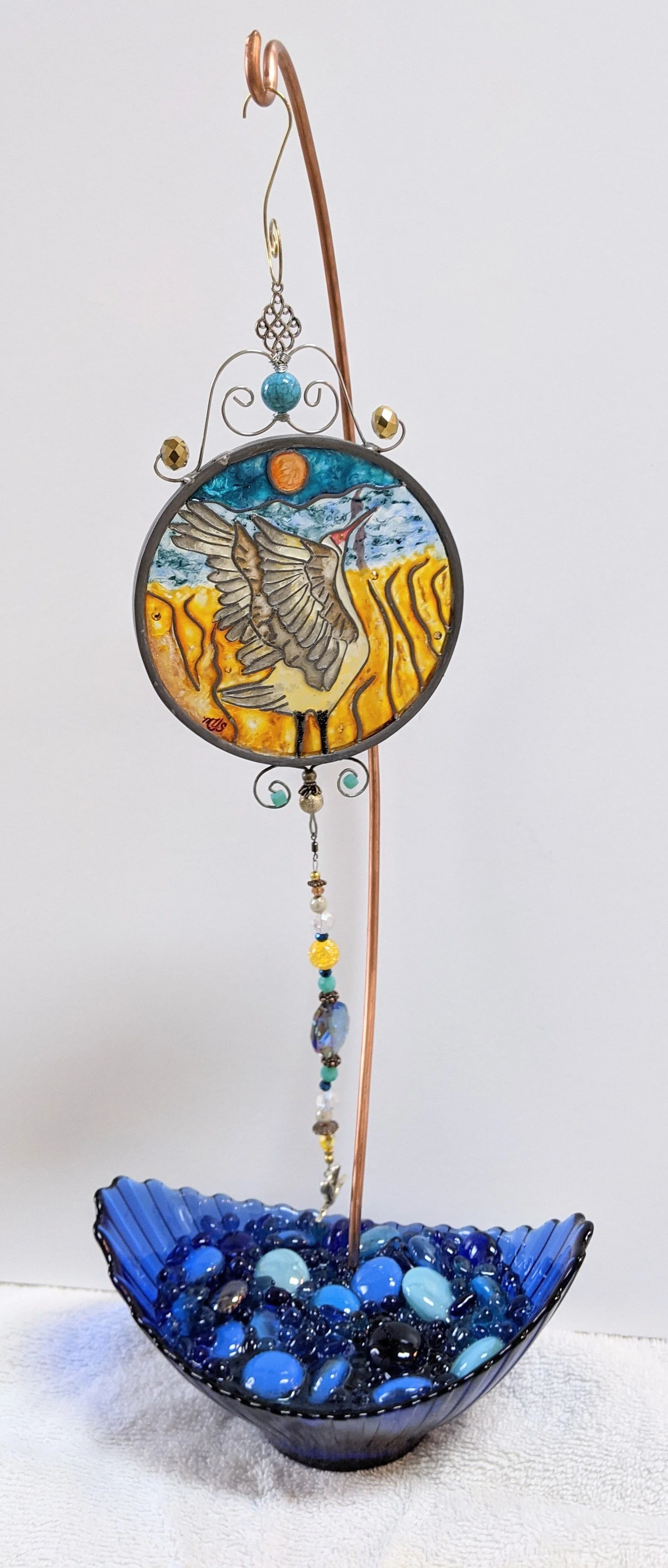 Sandhill Crane Illusion Glass on Blue Display Stand
This graceful display stand features a rich blue glass leaf-shaped base filled with sparkling blue and white stones, paired with an elegant hand-twisted copper rod. It beautifully supports a luminou