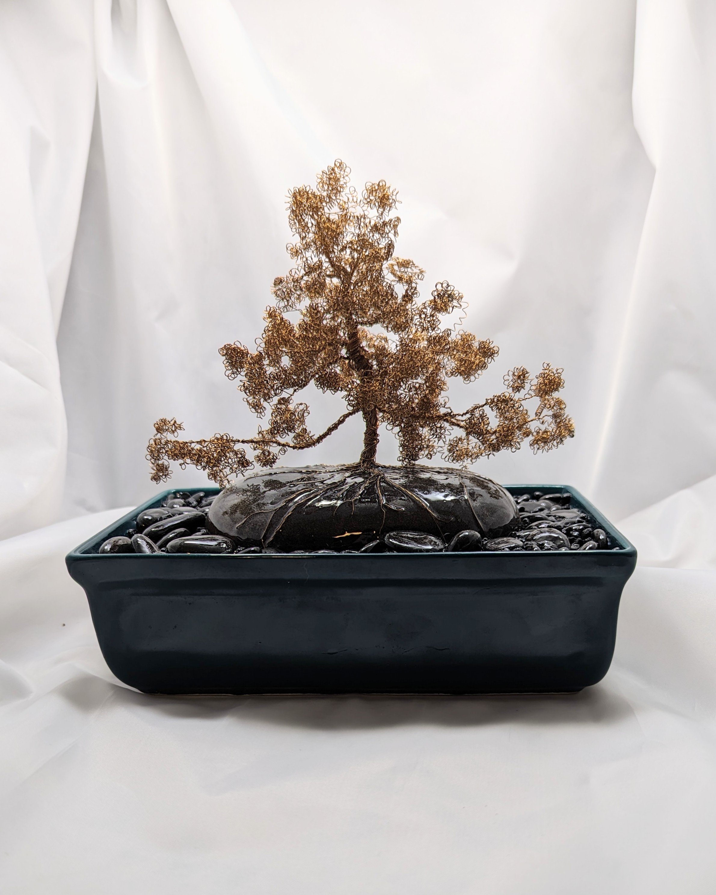 Golden Harmony on Ancient Stone bonsai diorama by Art Illusions by Young. Warm brass wire tree with golden foliage on dark stone base with river pebbles, moss, and black epoxy water. 110 hours work.