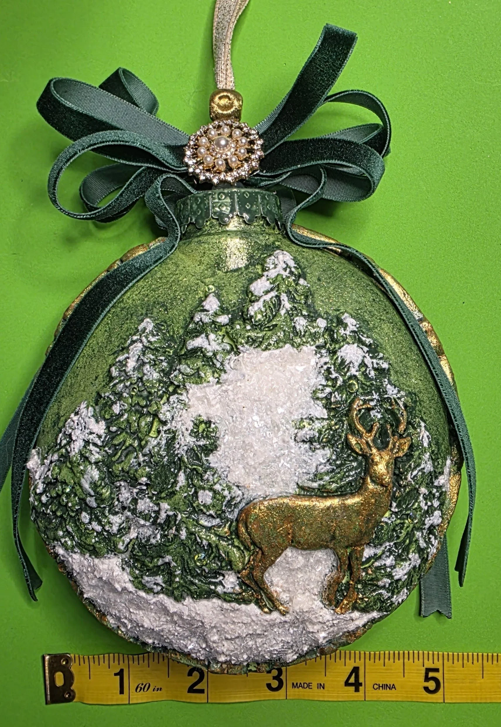 Detailed measurement of the Woodland Majesty Ornament by Art Illusions by Young. The noble stag and textured woodland elements are rendered with meticulous metallic green and gold finishes, creating lifelike depth and a sense of serene forest twiligh