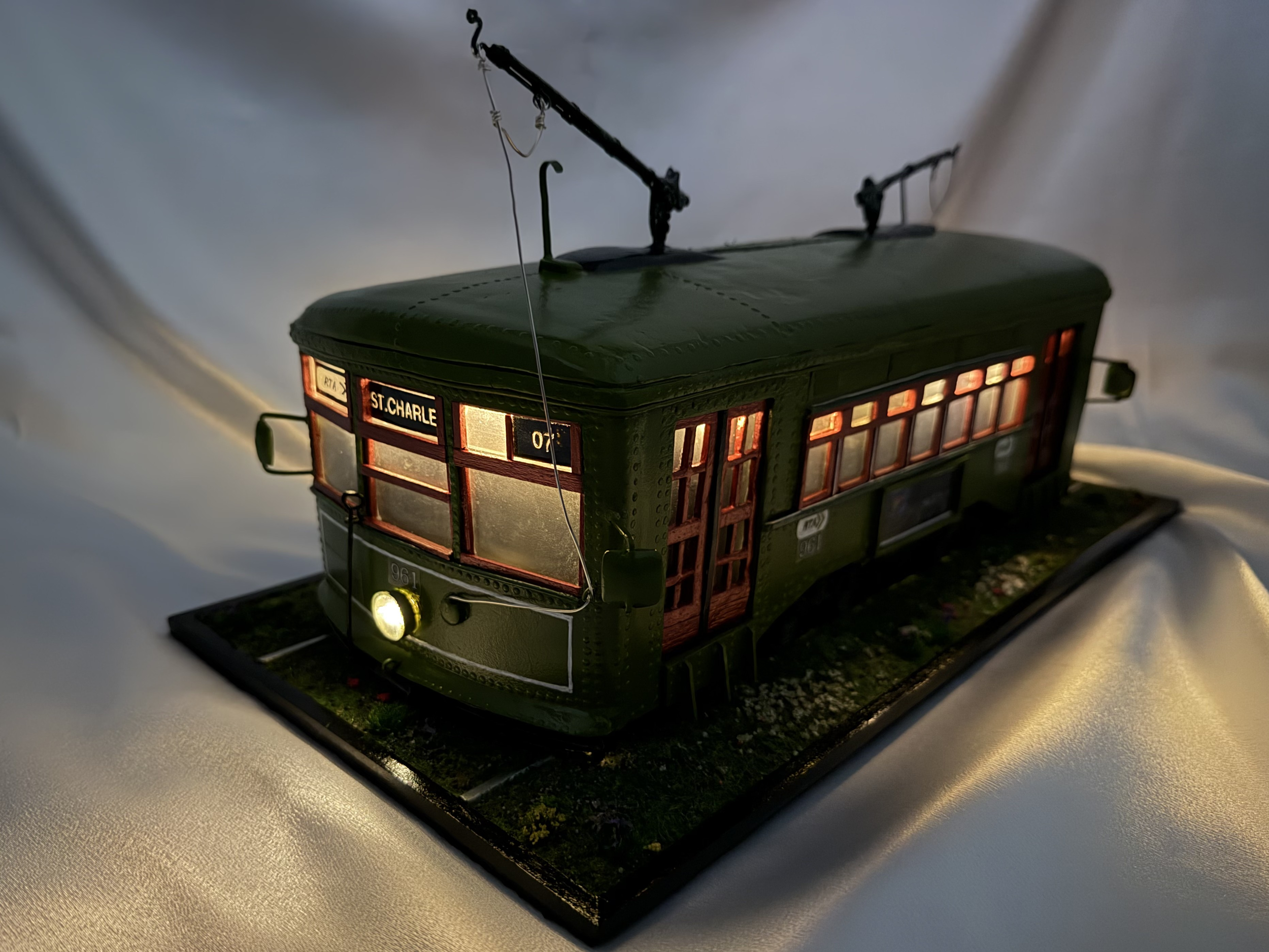 Side view of the illuminated black New Orleans streetcar artwork with glowing windows and interior lights. Handcrafted mixed media functional diorama by Art Illusions by Young.