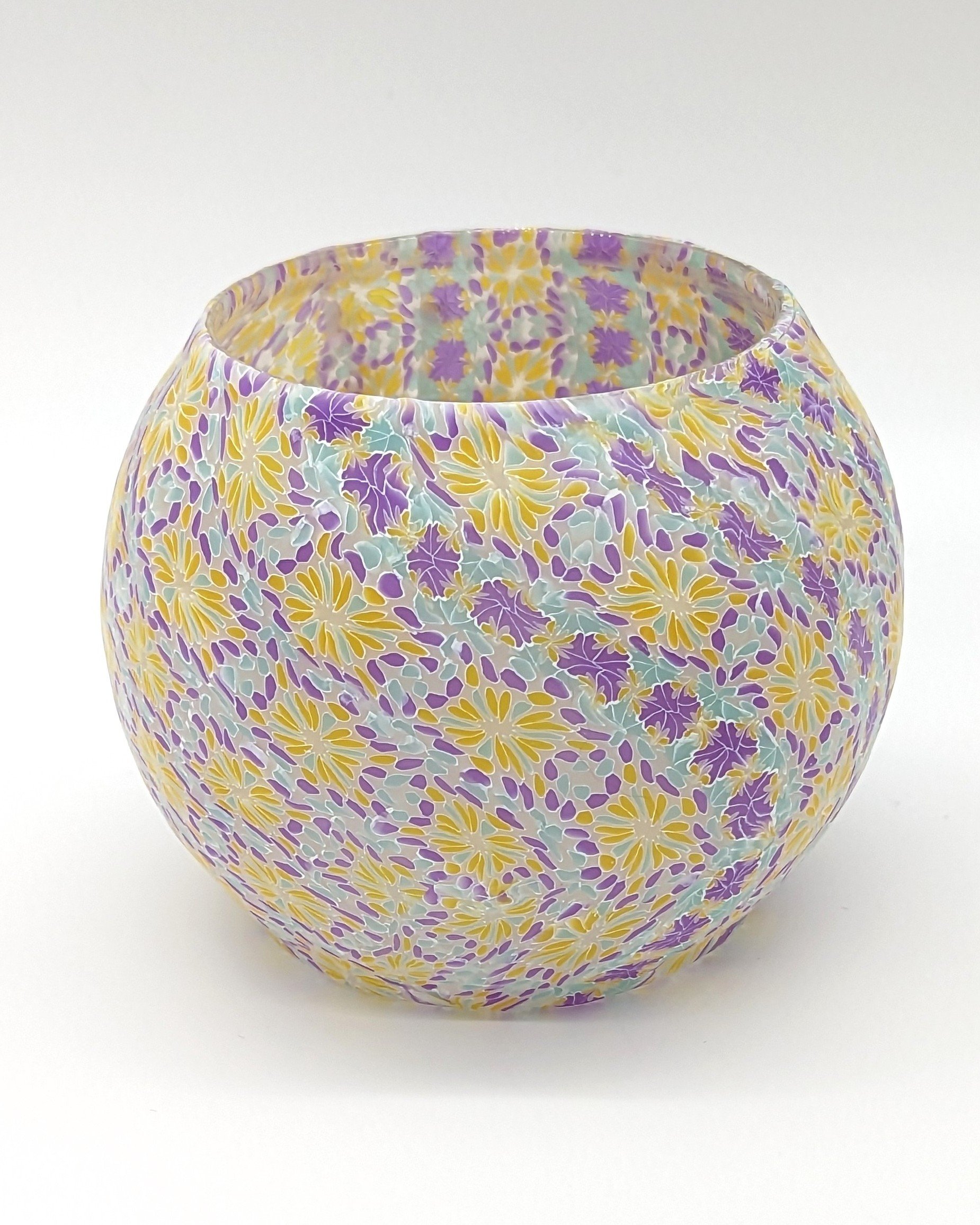 Another view of the Translucent Floral Candle Holder by Art Illusions by Young. Swirling, petal-like designs in layered colorful translucent polymer clay reveal subtle shifts in purple, gold, and aqua hues as light passes through the glass core. This