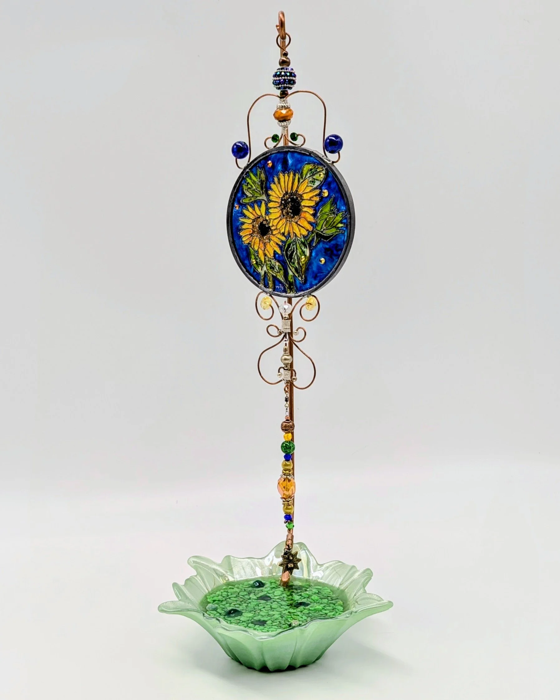Sunflower Illusion Glass on Handcrafted Display Stand
This vibrant display stand features a delicate green glass leaf-shaped base paired with an elegantly twisted copper rod. It beautifully supports a luminous Illusion Glass medallion bursting with g