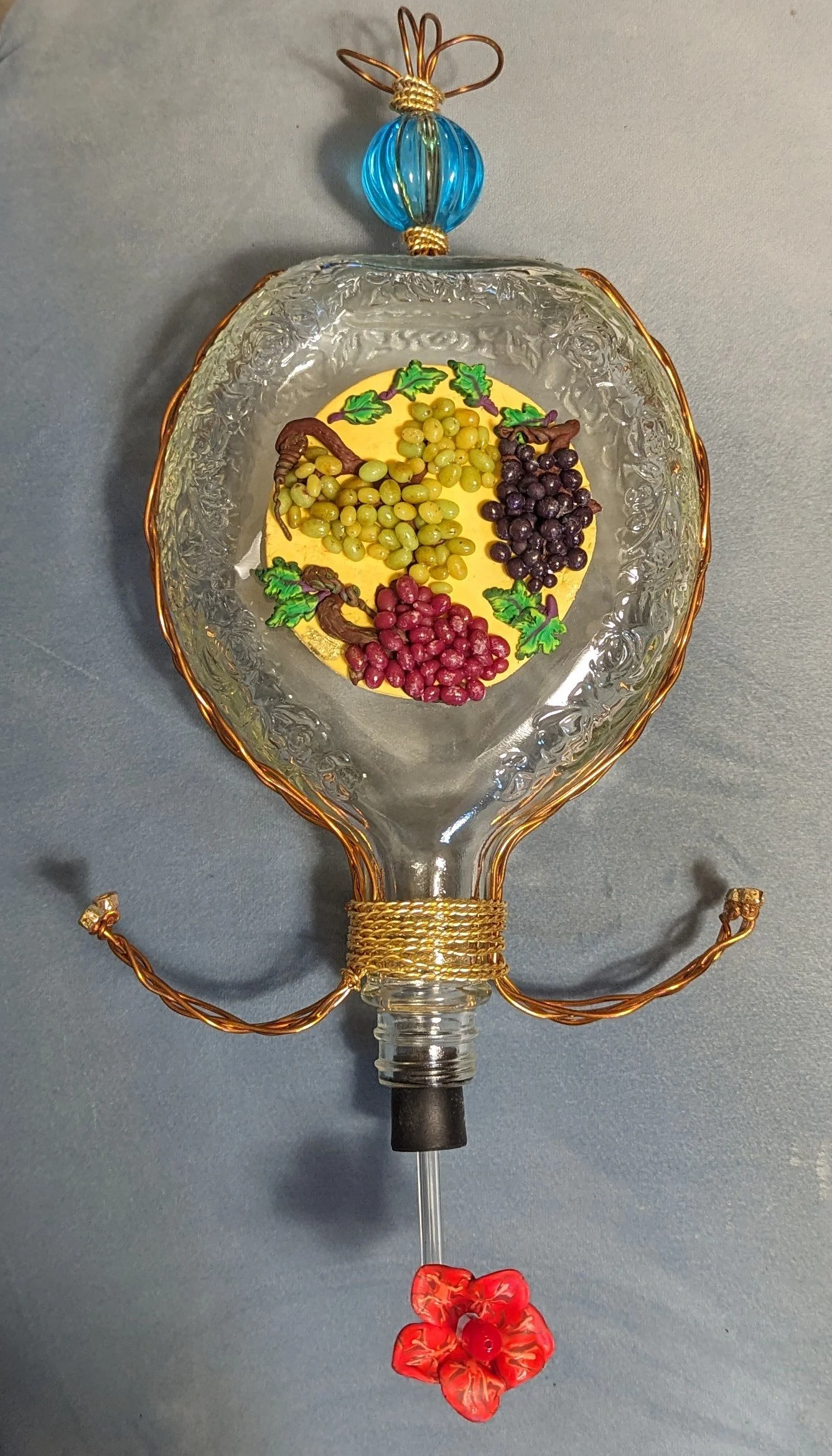 🔴 Sold: 
Grape Cluster Hummingbird Feeder by Art Illusions by Young, Folsom, Louisiana. A whimsical and artistic repurposed decorative spirits bottle transformed into a hummingbird feeder, featuring a vibrant hand-painted or sculpted grape cluster i