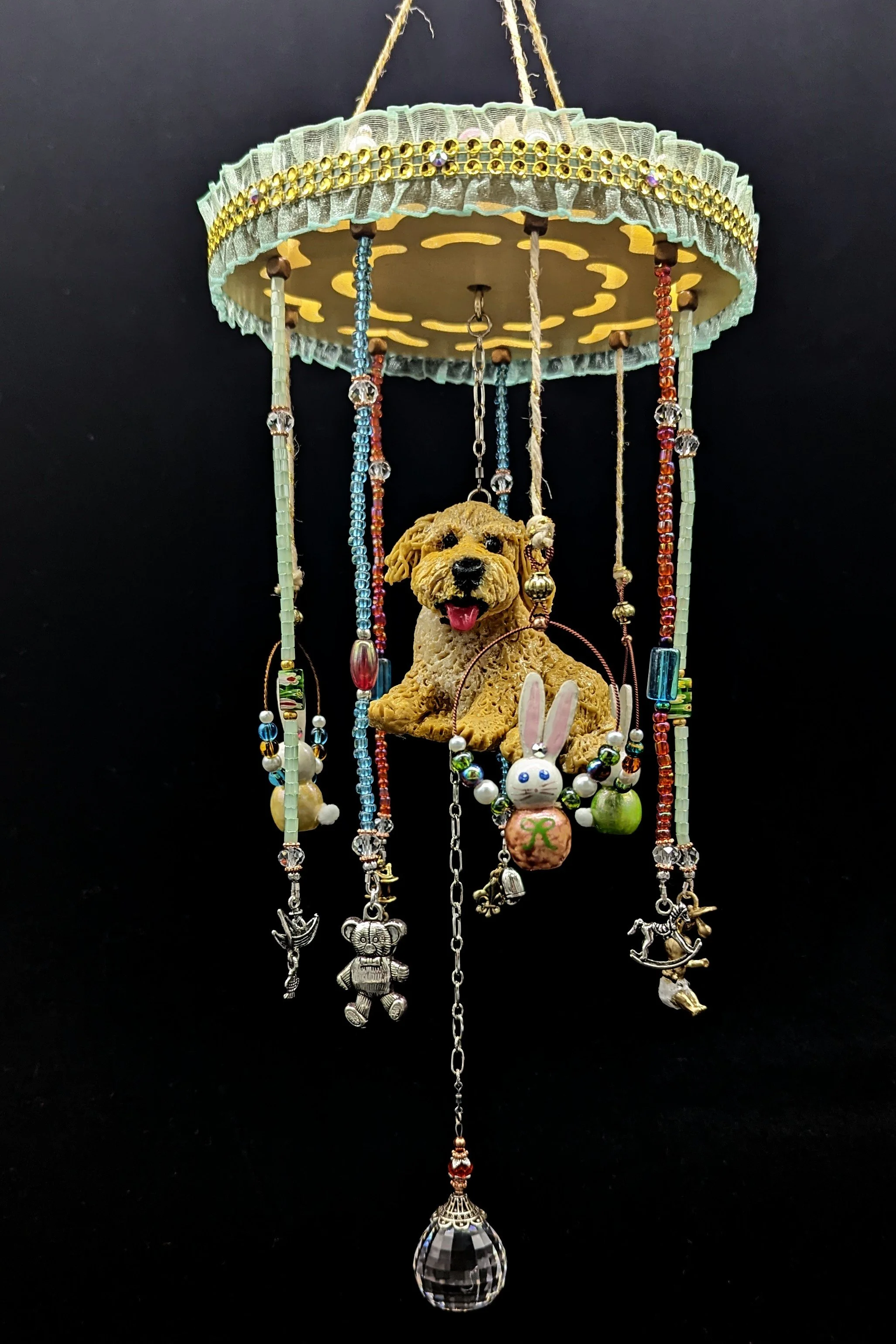 Close-up of the Puppy Commission Mobile by Art Illusions by Young on a black background. The hand-sculpted polymer clay Puppy sits prominently beneath the painted and decorated wooden hanger. Six specially selected charms and a large 58mm round facet