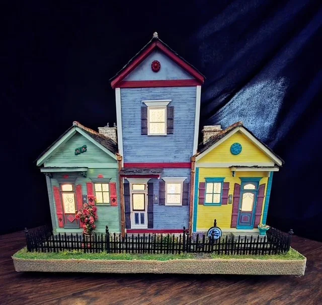 Rear nighttime view of the handcrafted Triple New Orleans Shotgun House Row diorama by Art Illusions by Young. Illuminated from within, the warm interior lighting glows through the windows and transoms of all three shotgun houses, highlighting the de