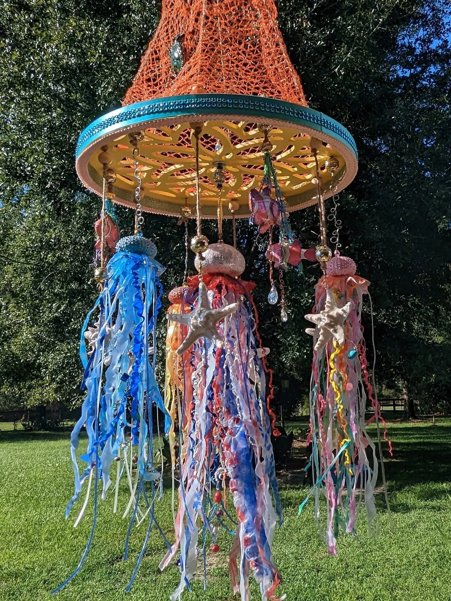 Close-up detail of the Nautical Jellyfish Mobile by Art Illusions by Young. The decorative netted canopy and scrollwork wooden hanger support four miniature sea urchin jellyfish with flowing tentacles and iridescent details, alongside embellished res