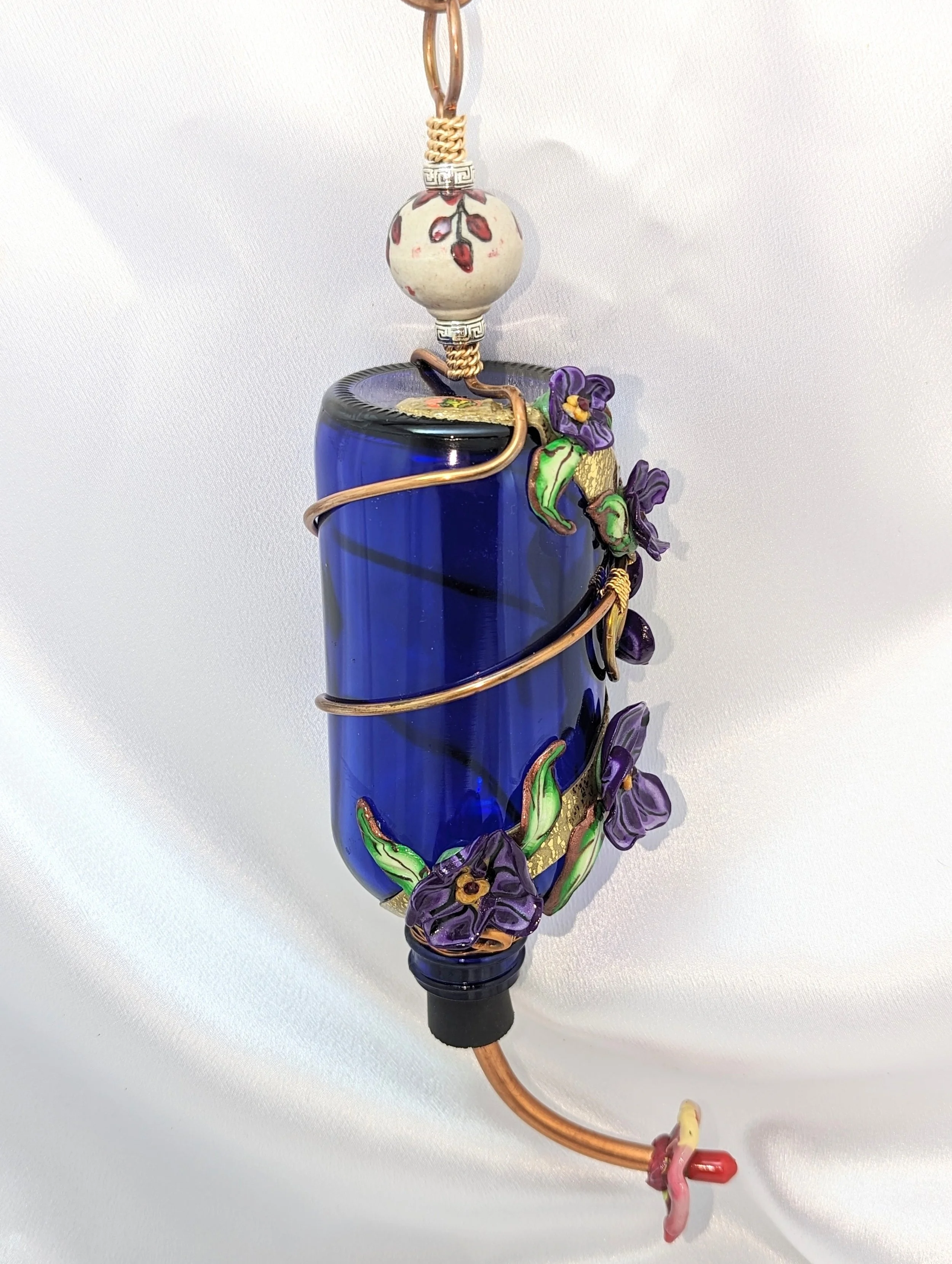 Purple Pansy Hummingbird Feeder by Art Illusions by Young. Handcrafted with a blue glass bottle, purple polymer clay pansy flowers, and copper wire accents.