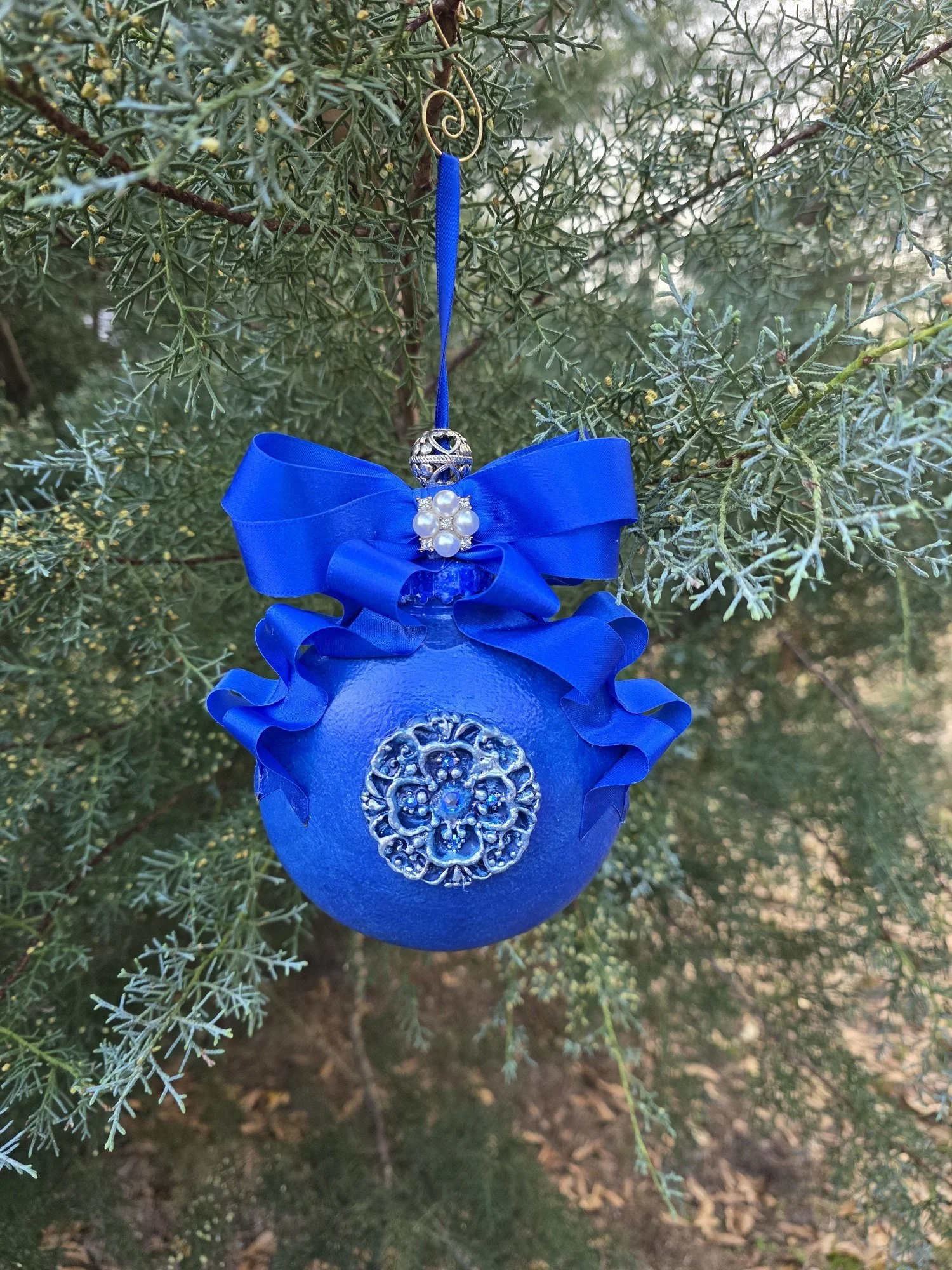Rear hanging view of the Royal Blue Cross Ornament by Art Illusions by Young. The hand-painted cobalt blue form and raised silver medallion with is visible, complemented by the dramatic ribbon bow. The subtle metallic sheen and intricate detailing cr