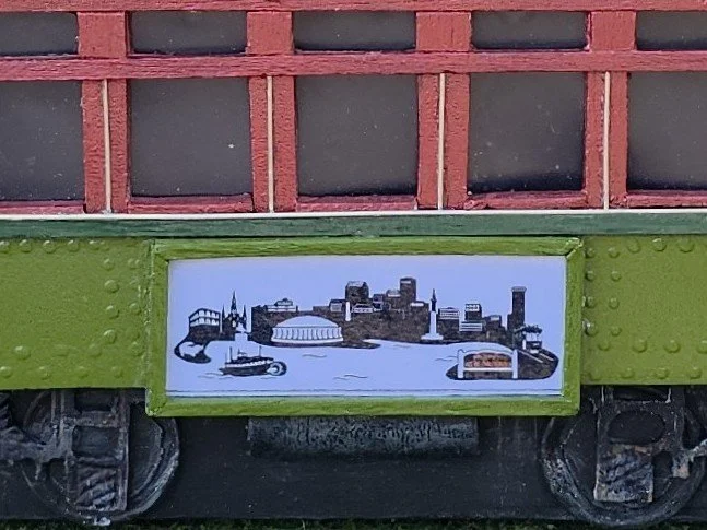 Detail shot of the red window section and cityscape advertisement on the New Orleans St. Charles streetcar tissue box cover. Intricate hand-painted details in this functional mixed media piece by Art Illusions by Young.