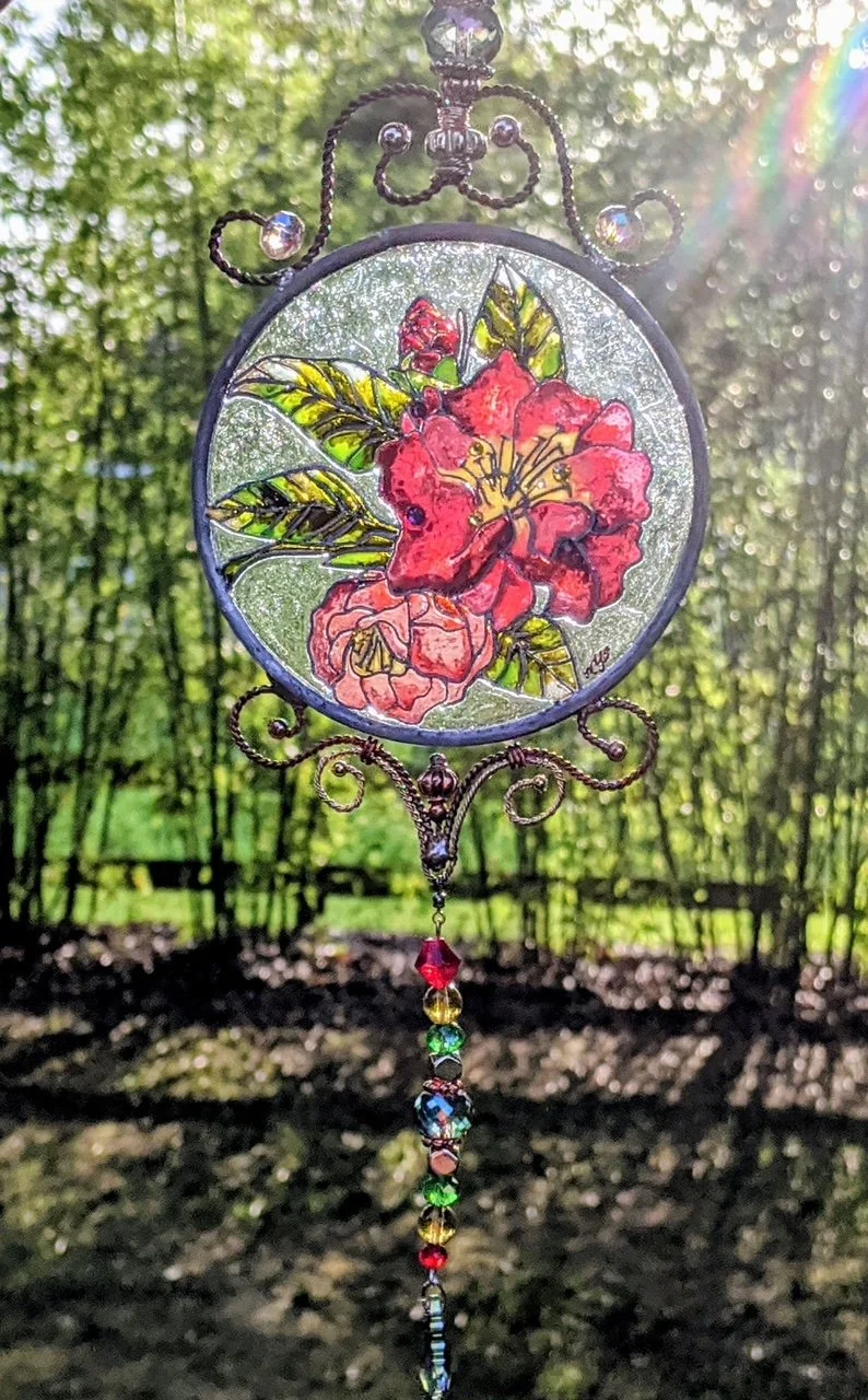🔴 Sold: 
Red Camellia Illusion Glass by Art Illusions by Young. A lush red camellia with deep green leaves fills this round suncatcher, its petals rendered with rich color and delicate shading. The fragrant Southern flower glows with warmth and soph