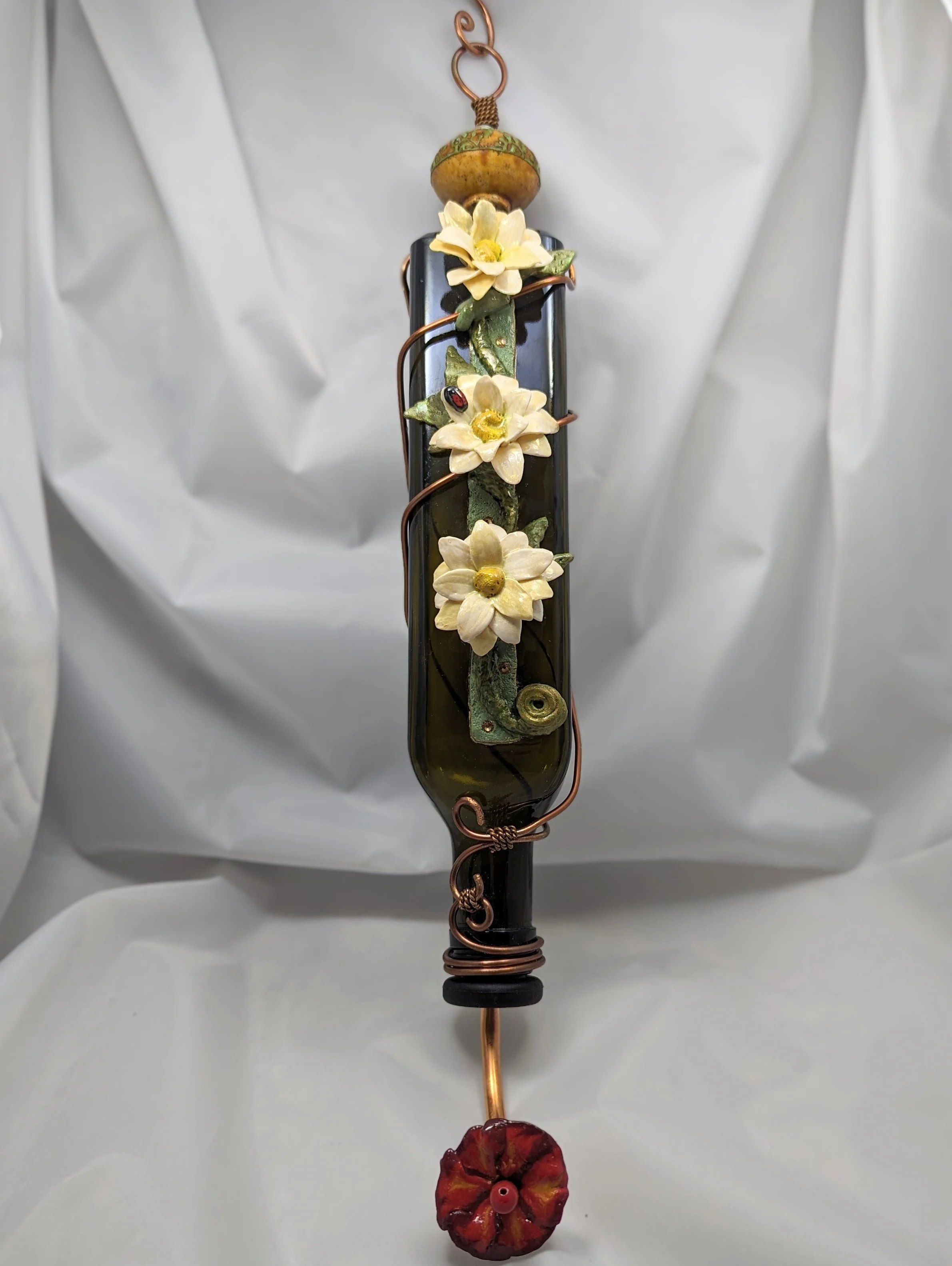 White Daffodil Elegance Hummingbird Feeder by Art Illusions by Young from Folsom, Louisiana. A recycled dark green glass bottle is elegantly transformed with intricate copper wire wrapping shaped into graceful vines and tendrils, adorned with hand-sc