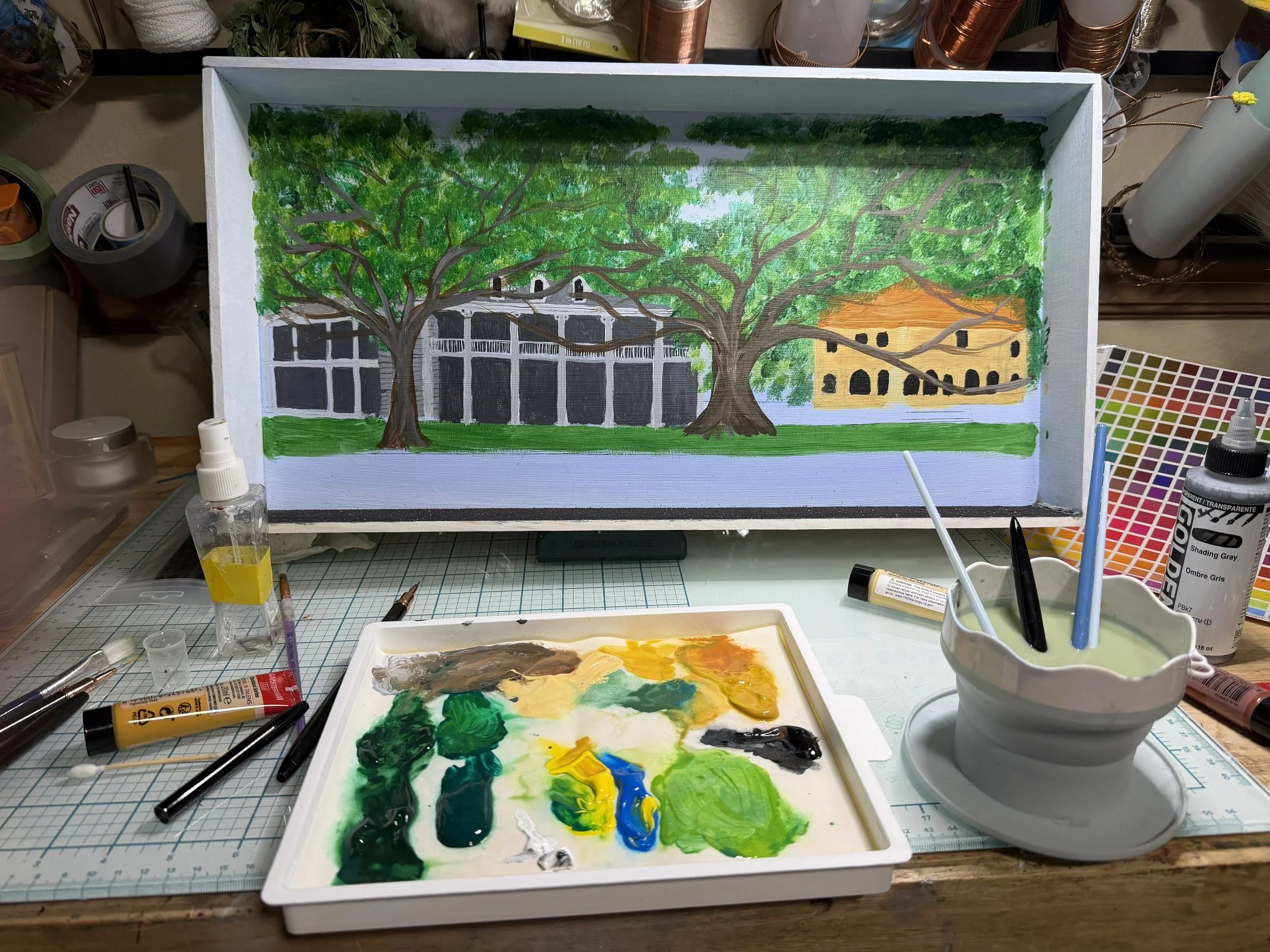 Behind-the-scenes studio view of the King Rex Mardi Gras float diorama in progress, showing the white display box and artist’s painting palette. Creation process by Art Illusions by Young.