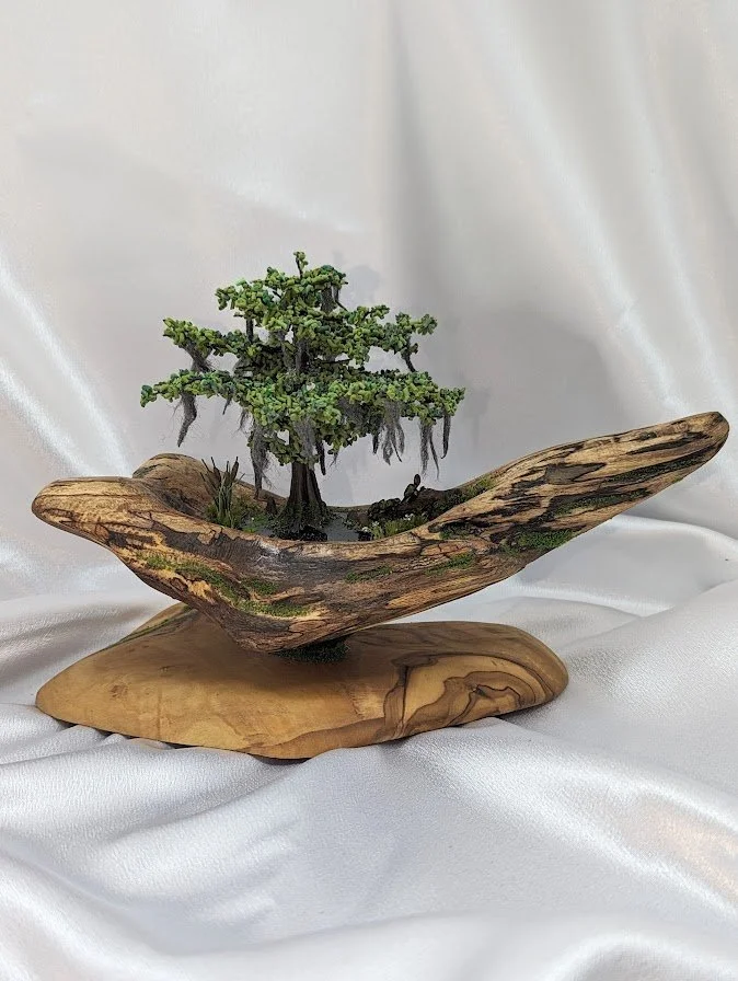 🔵  Donated: 
Cypress Bonsai on Driftwood Diorama by Art Illusions by Young, Folsom, Louisiana. This miniature bonsai-style cypress tree is meticulously sculpted, then mounted on a natural driftwood base with Spanish moss accents. The piece captures 