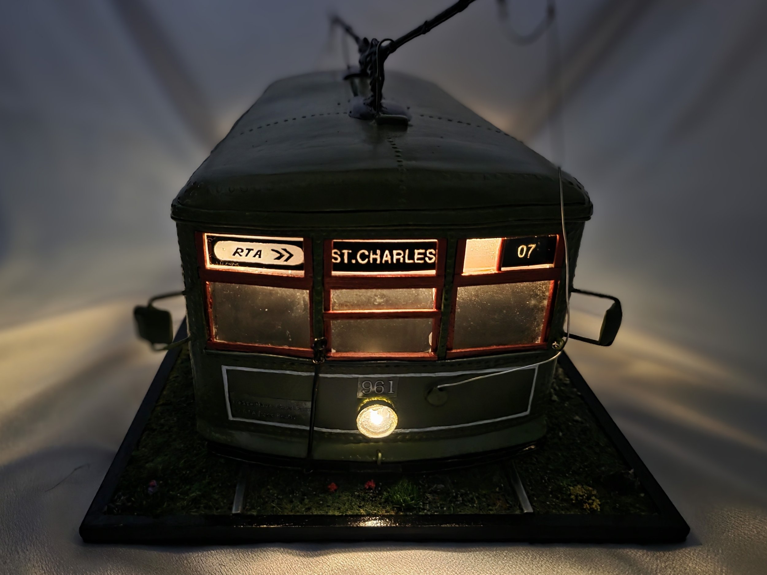 Illuminated front view of the black New Orleans streetcar diorama showing glowing interior LED lights, headlight, and detailed windows. Dramatic night-time presentation of the functional tissue box cover by Art Illusions by Young.