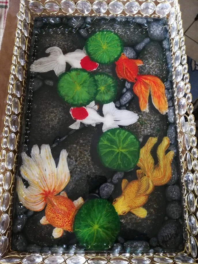 Fantail Goldfish Pond wall piece by Art Illusions by Young, Folsom, Louisiana. Hand-painted koi and fantail goldfish swimming among green lily pads and rocks on a dark background, sealed in clear epoxy for luminous depth and archival quality.