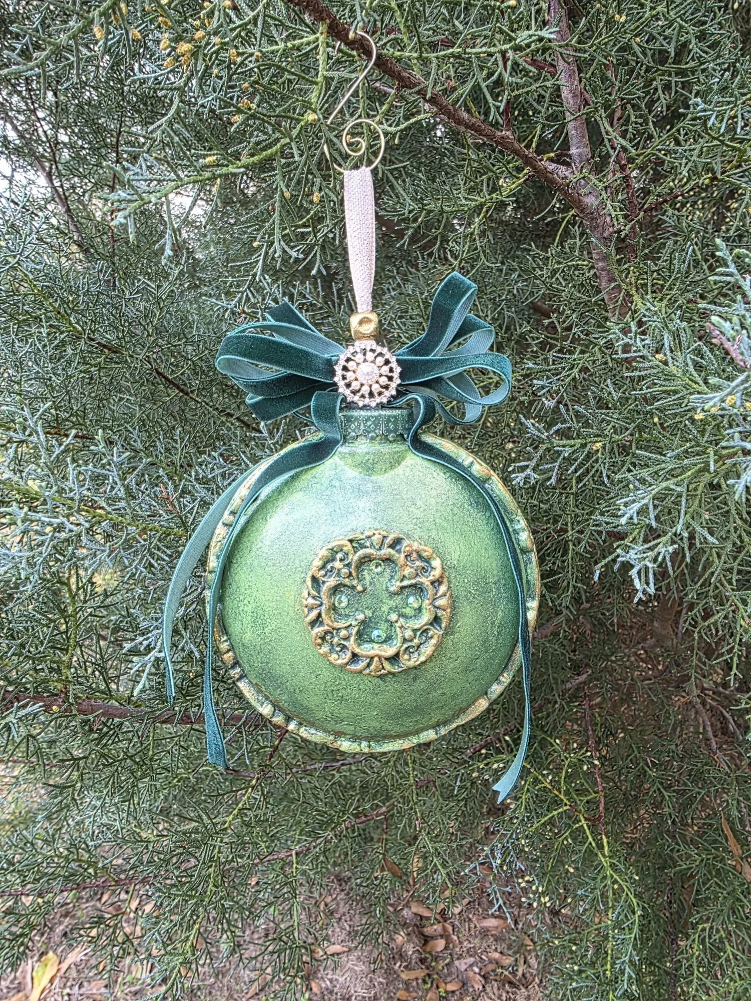 Display view of the Woodland Majesty Ornament by Art Illusions by Young. The three-dimensional hand-sculpted stag and surrounding pines are visible from this perspective, with metallic green and gold finishes capturing lifelike depth and texture. The