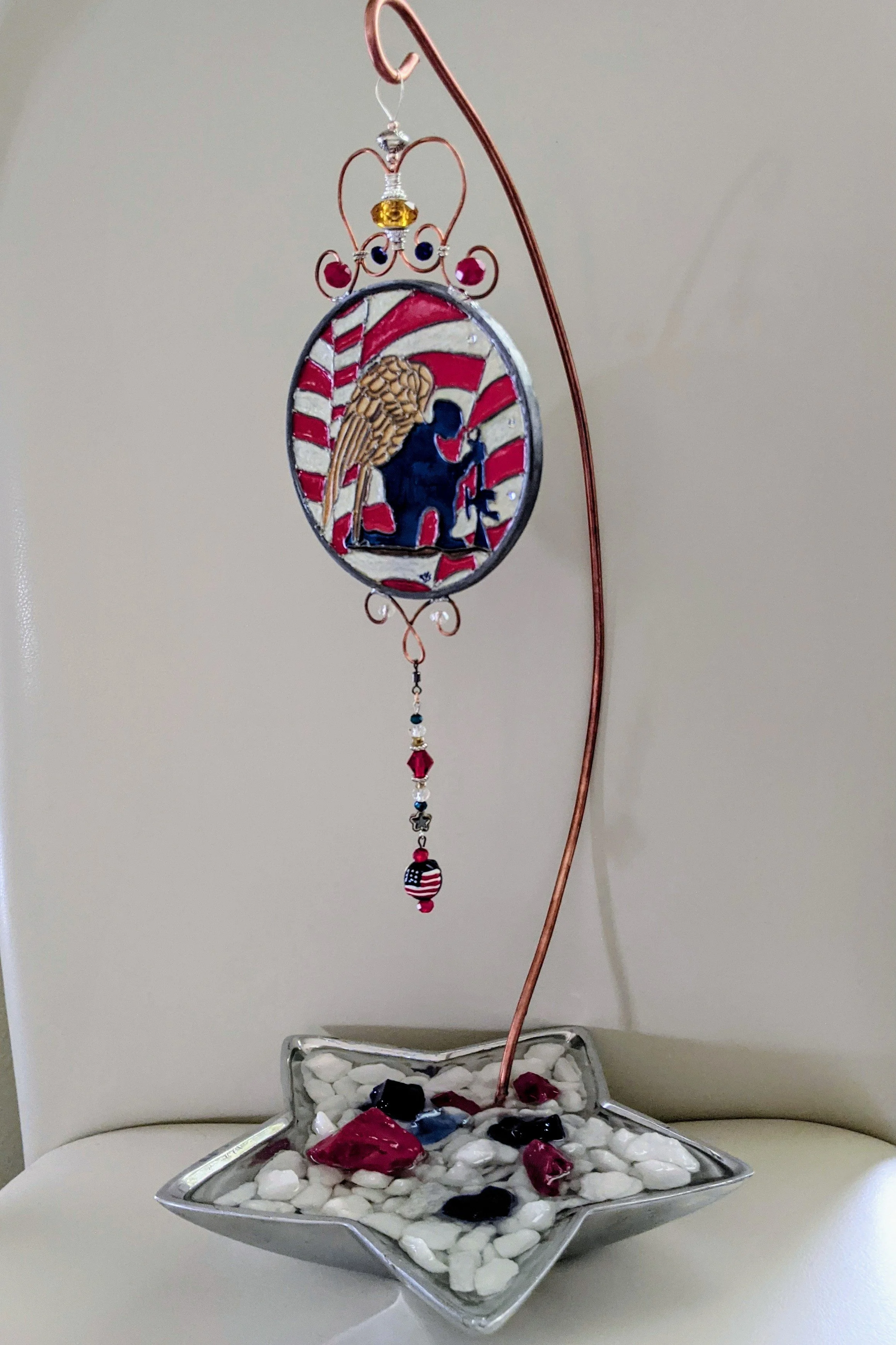 Handcrafted Display Stand with Patriotic Guardian Angel  Soldier Ornament
This elegant display stand features a metal star-shaped base filled with a sparkling mix of white, red, and blue stones, paired with a graceful, hand-twisted copper rod. The st