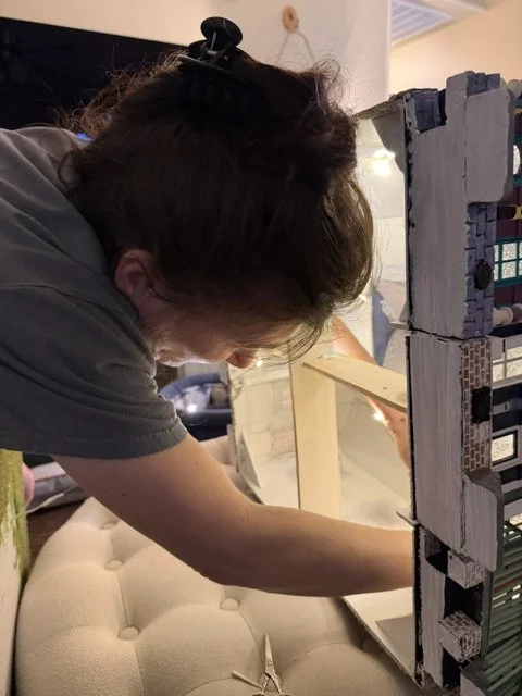 Behind-the-scenes view of artist Sandra Young meticulously installing the interior lighting in the Triple New Orleans Shotgun House Row diorama at Art Illusions by Young. This intimate moment captures the extraordinary dedication and precision requir