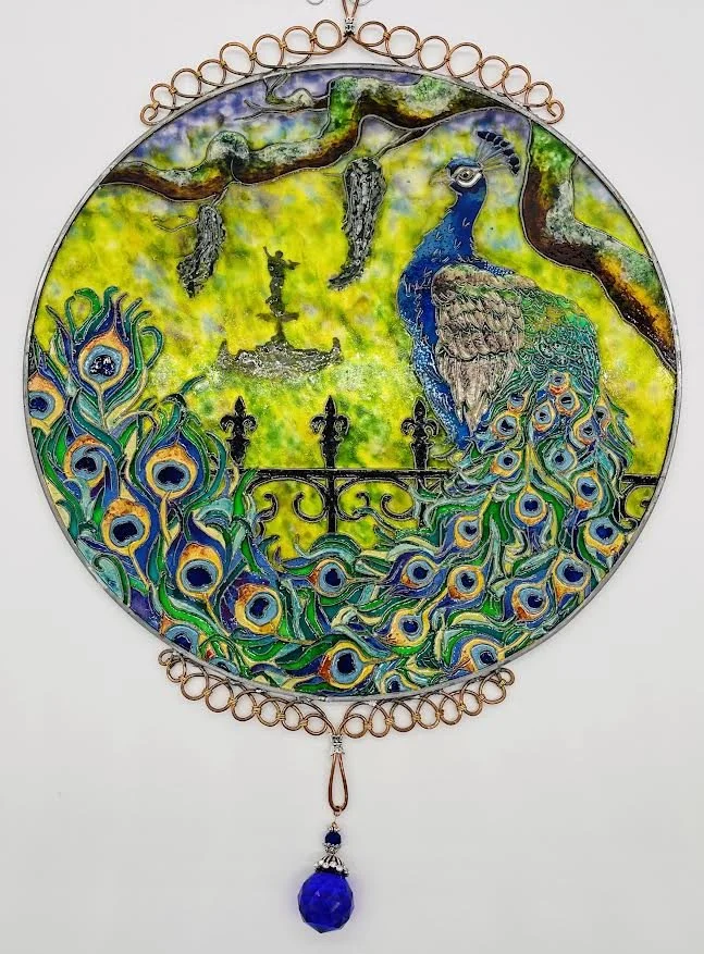 🔴 Sold: 
Peacock in the Garden Illusion Glass by Art Illusions by Young, Folsom, Louisiana. This luminous circular suncatcher captures a majestic peacock displaying its iridescent tail feathers amid lush greenery and golden accents. Hand-painted wit