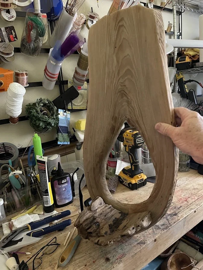 Behind-the-scenes studio view of the Enchanted City Park Serenity diorama in progress, showing the large hollow cypress tree trunk surrounded by sculpting tools, paints, and materials. Creation process by Art Illusions by Young.