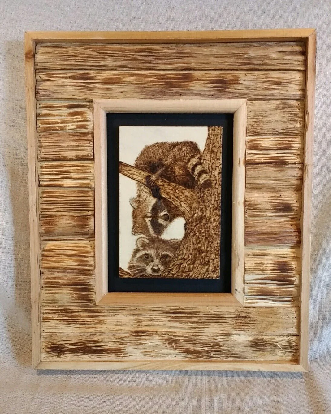 🔵Donated: Louisiana Society of Hearing Aid Specialists (LSHAS)
Playful Raccoons Pyrography by Art Illusions by Young, Folsom, Louisiana. This charming woodburn artwork features a pair of curious raccoons nestled among tree branches, one peeking out 