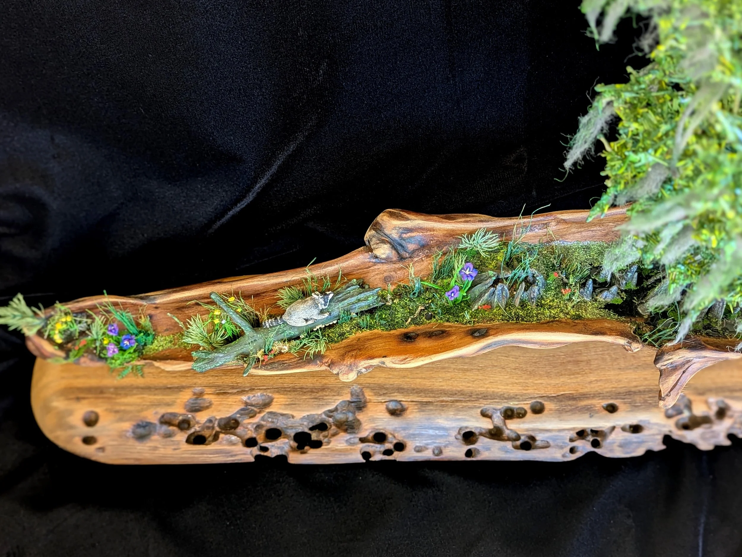 Angled view of a micro swamp diorama featuring a sculpted clay raccoon and irises, layered driftwood, hand-applied moss, wildflowers, and a subtle water channel. Handcrafted by Art Illusions by Young as part of the Micro Swamp / Bonsai series.