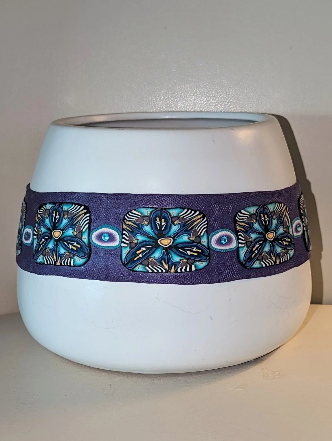 🔴 Sold: 
Polymer Clay Decorated Flower Pot by Art Illusions by Young. A charming white ceramic flower pot transformed with a wide band of hand-sculpted and painted polymer clay featuring blue and white floral motifs. The detailed work turns an ordin
