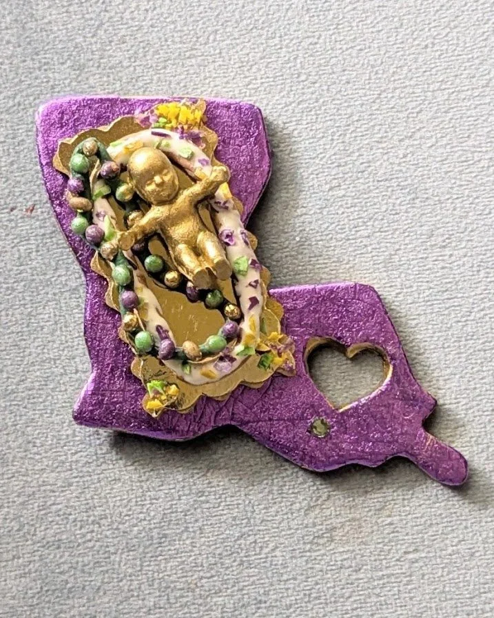 🔴 Sold: 
Mardi Gras Baby King Cake Magnet/Pin by Art Illusions by Young. A festive Mardi Gras baby figure adorned with colorful beads and gold accents, designed as both an magnet and pin. Hand-sculpted in polymer clay, it captures the playful tradit