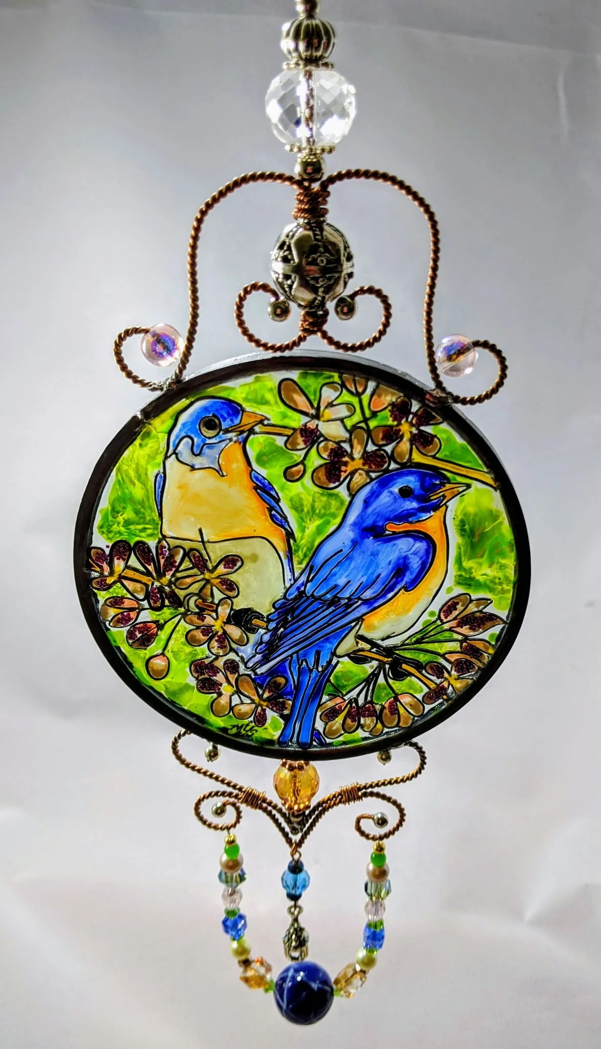 🔴 Sold: 
Bluebirds Illusion Glass Suncatcher by Art Illusions by Young, Folsom, Louisiana. This charming circular suncatcher captures a pair of vibrant bluebirds perched together on a branch amid soft green foliage and delicate blossoms. Hand-painte