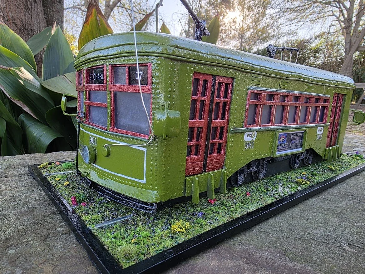 New Orleans St. Charles Streetcar diorama by Art Illusions by Young, Folsom Louisiana. Hand-sculpted olive green streetcar number 961 with red doors and windows, detailed signage, miniature tracks, and grassy base with wildflowers.