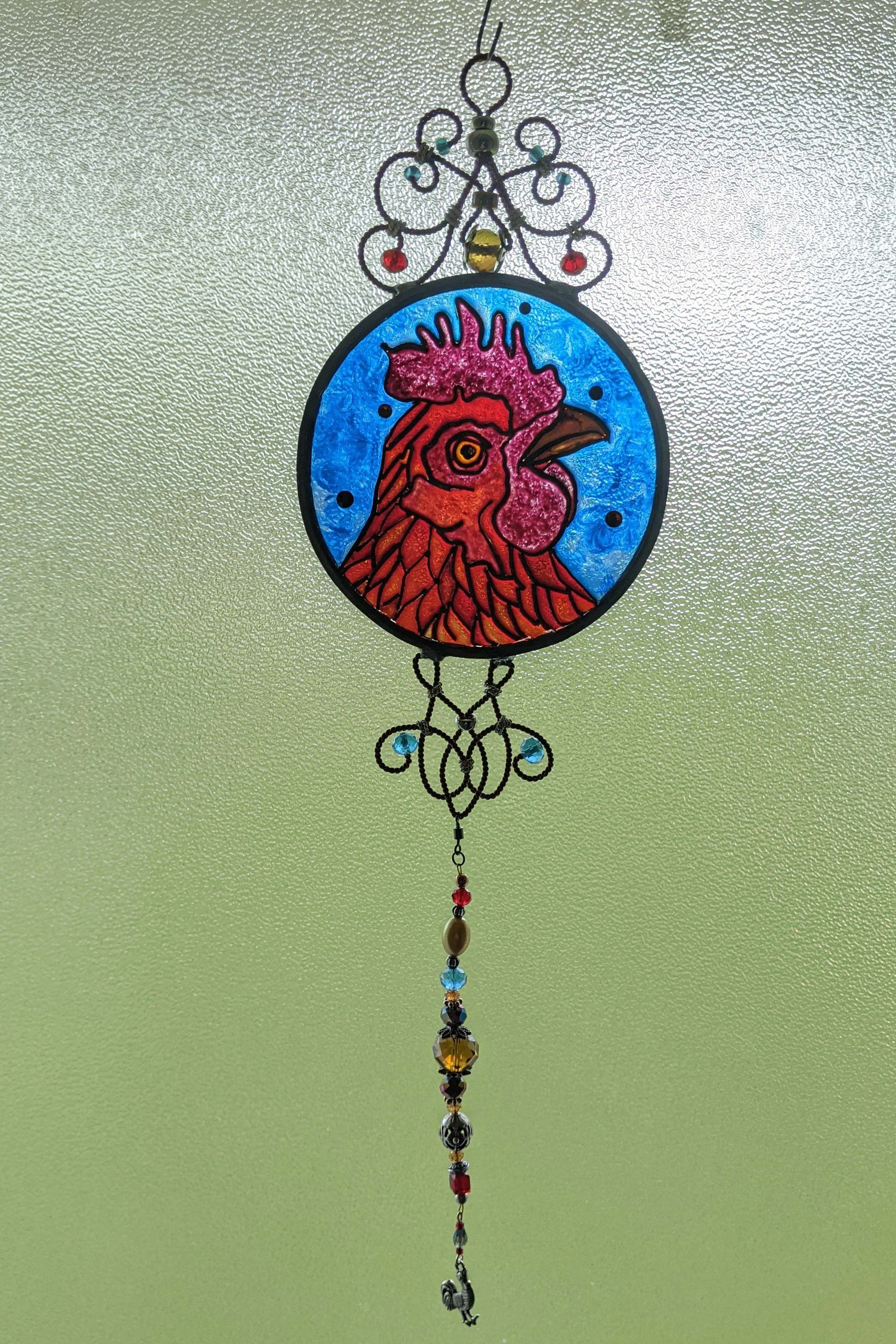 🔴 Sold: 
Rhode Island Red Chicken Illusion Glass by Art Illusions by Young. A bold circular suncatcher portraying a proud Rhode Island Red rooster with rich red plumage against a textured blue background. The detailed hand-painted work brings farmya