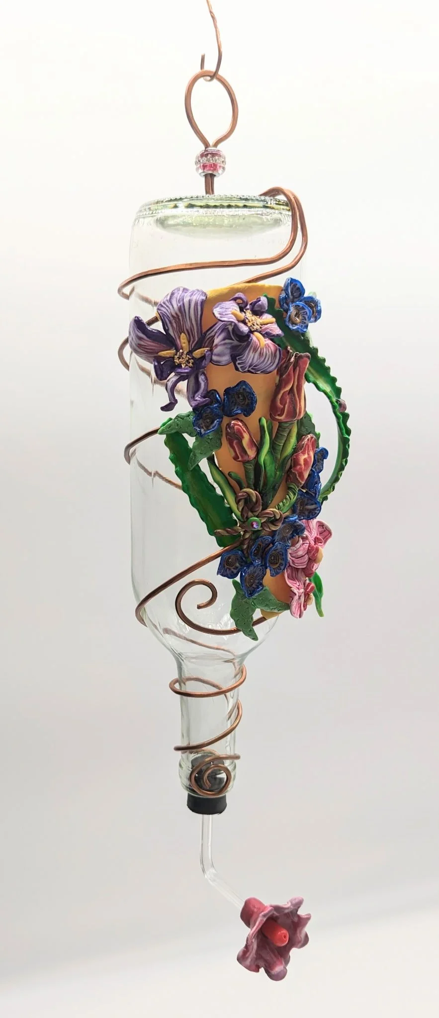 🔴 Sold: 
Purple Iris Hummingbird Feeder by Art Illusions by Young, Folsom, Louisiana. A clear recycled glass bottle elegantly decorated with hand-sculpted polymer clay purple irises and lush green foliage, accented by flowing copper wire swirls. Thi