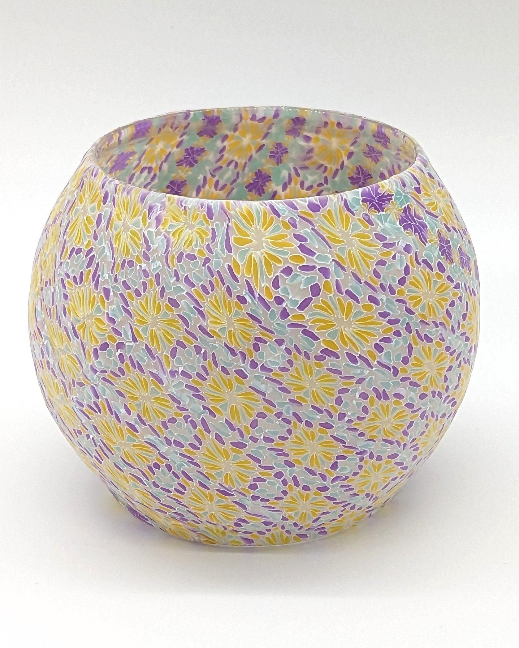 Detailed angled view of the Translucent Floral Candle Holder by Art Illusions by Young. The hand-layered colorful translucent clay displays intricate floral motifs and swirling patterns that filter light in a magical, stained-glass manner. Vibrant ye