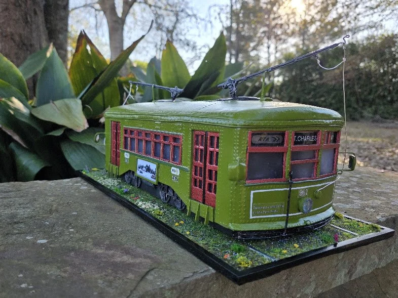 Angled view of the New Orleans St. Charles streetcar diorama on its handcrafted base with wildflowers and tracks. One-of-a-kind functional tissue box cover with LED lighting by Art Illusions by Young.