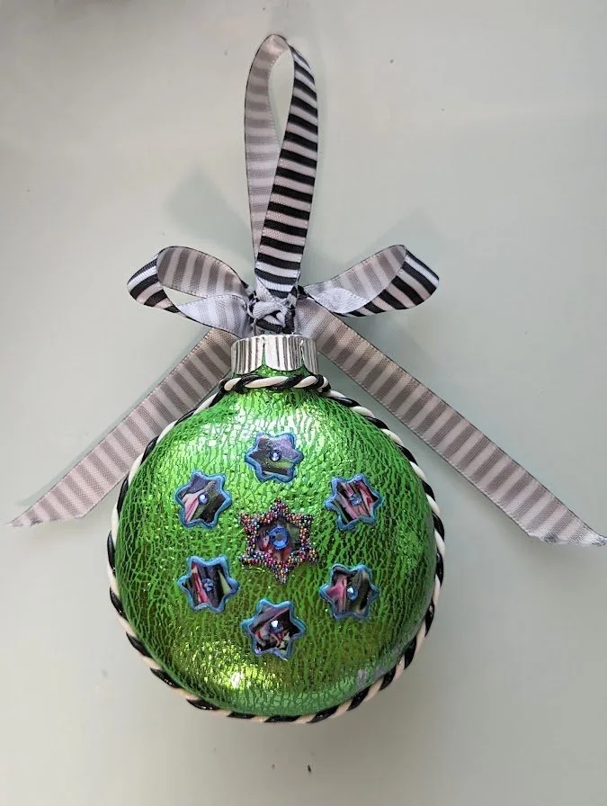 🔴 Sold: 
Green Christmas Ornament by Art Illusions by Young. A vibrant green spherical ornament adorned with delicate floral and bead-like accents in purple and blue tones. The hand-sculpted polymer clay surface glows with holiday cheer and meticulo