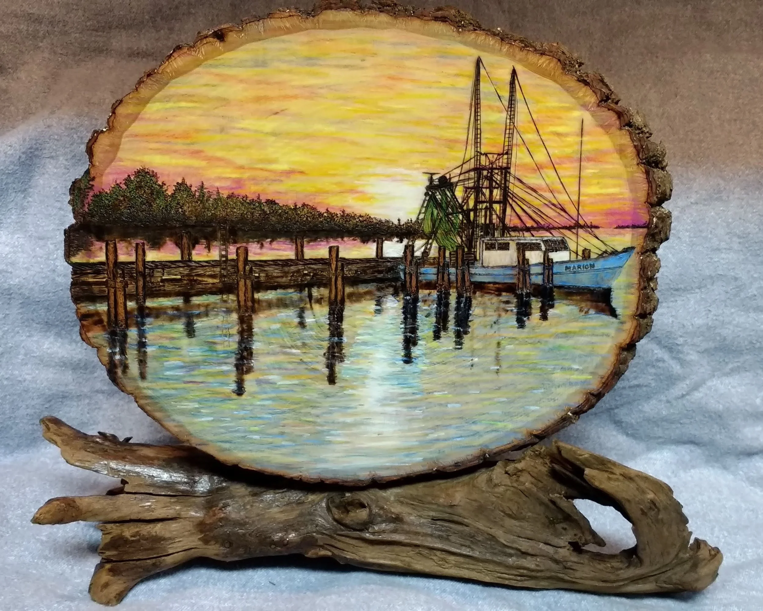 🟢 Available : 
Nostalgic pyrography (woodburned) sunset scene of the historic Bucktown fishing village in New Orleans by Art Illusions by Young. The old village is rendered on a circular basswood crosscut with layered inks, watercolors, and colored 