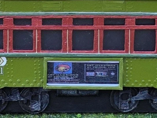 Close-up detail of the side advertisement panel on the New Orleans streetcar diorama, featuring custom Art Illusions by Young signage and realistic city elements. Hand-painted mixed media art.