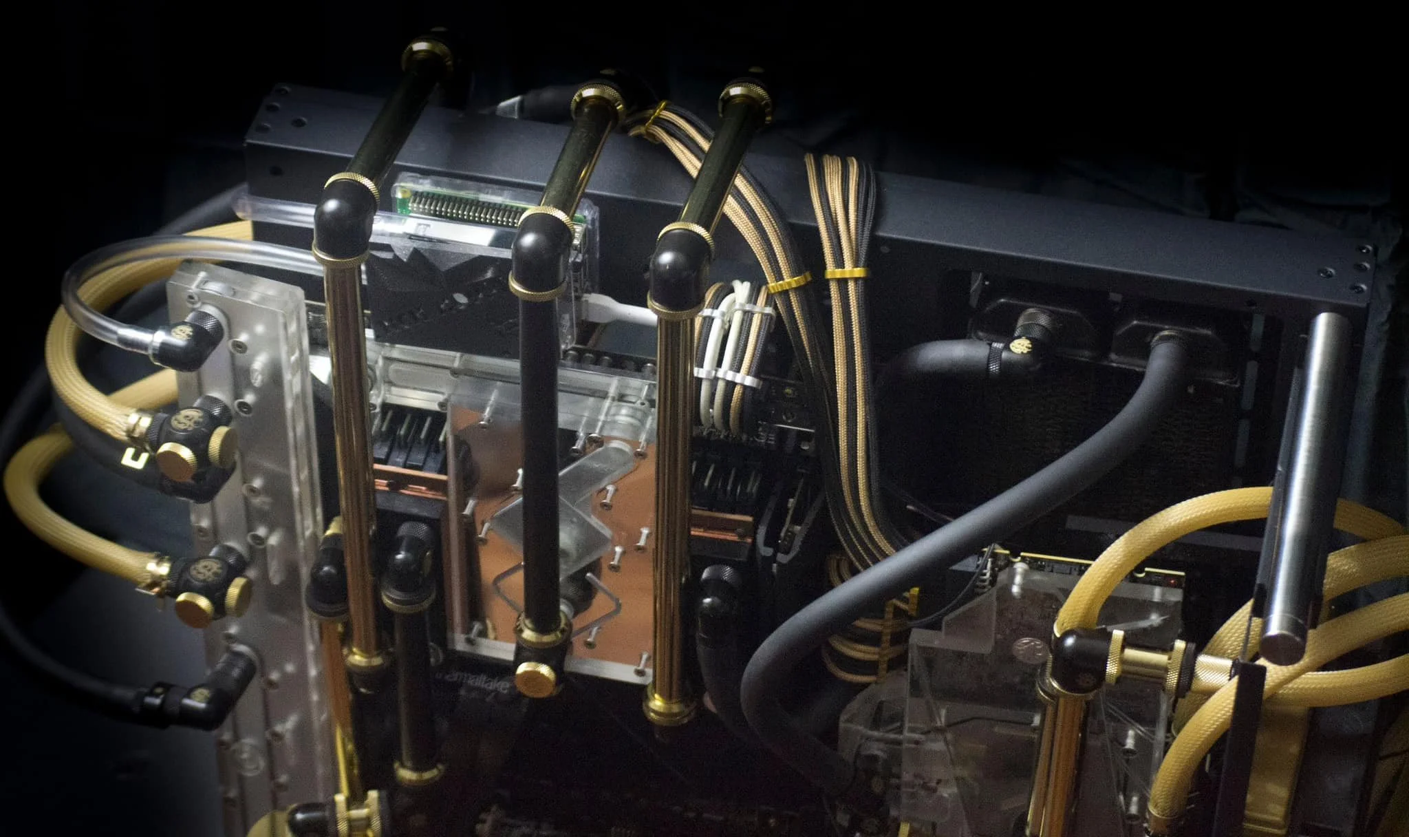 Close-up of a custom computer water cooling system with black and gold tubing, fittings, and a radiator.