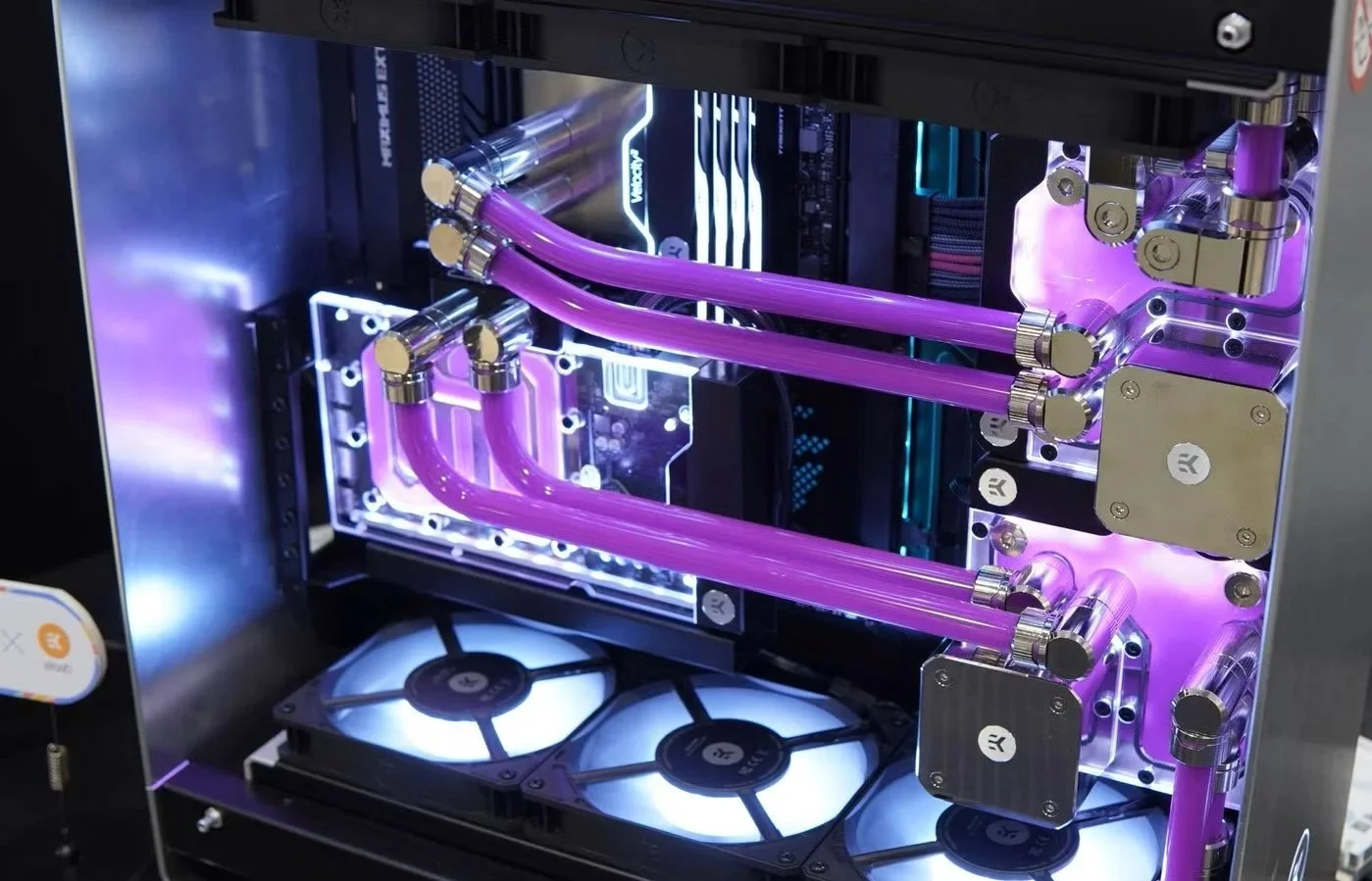 A custom-built gaming or high-performance computer with a liquid cooling system. The system features purple coolant tubes, illuminated cooling blocks, and cooling fans with blue lighting inside a metallic case.