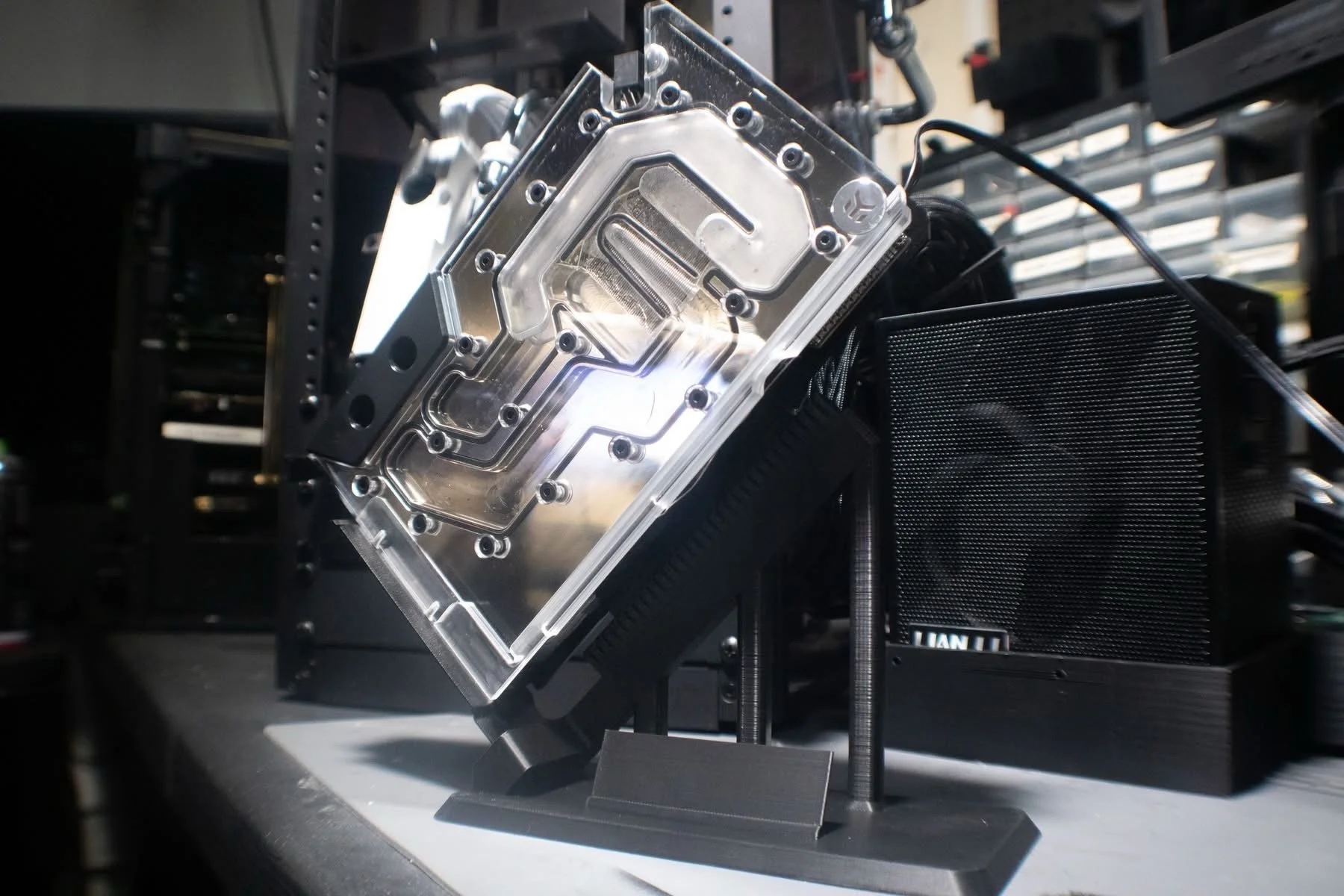 Close-up of a computer cooling block with water channels, mounted on a black frame with cables connected to it, in a technical setup or lab environment.