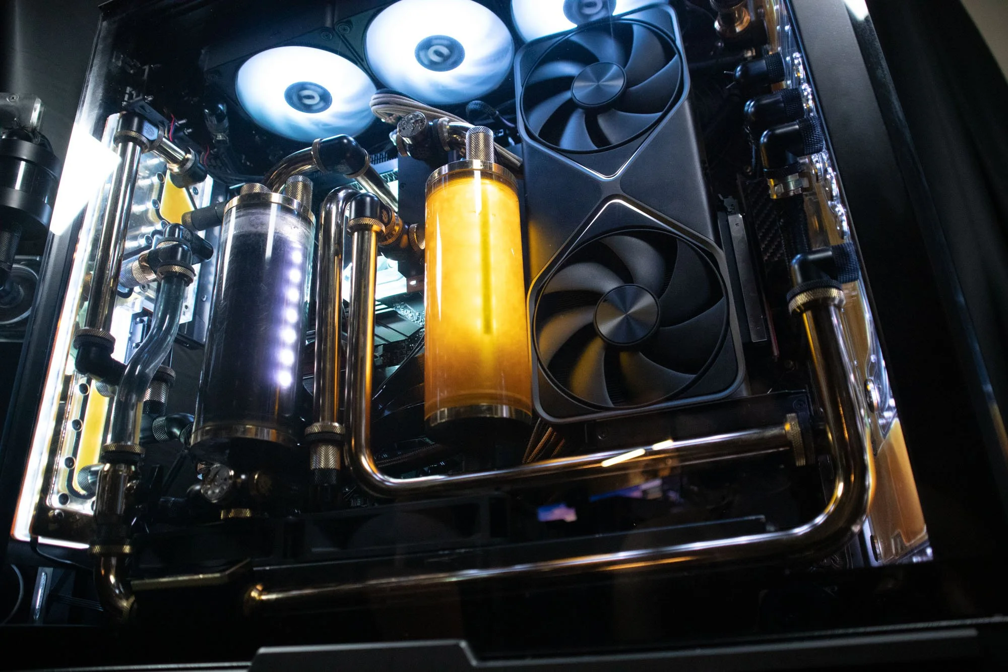 Inside a high-end custom computer with liquid cooling system, featuring tubes, reservoirs with yellow and black liquids, cooling fans, and a graphics card.